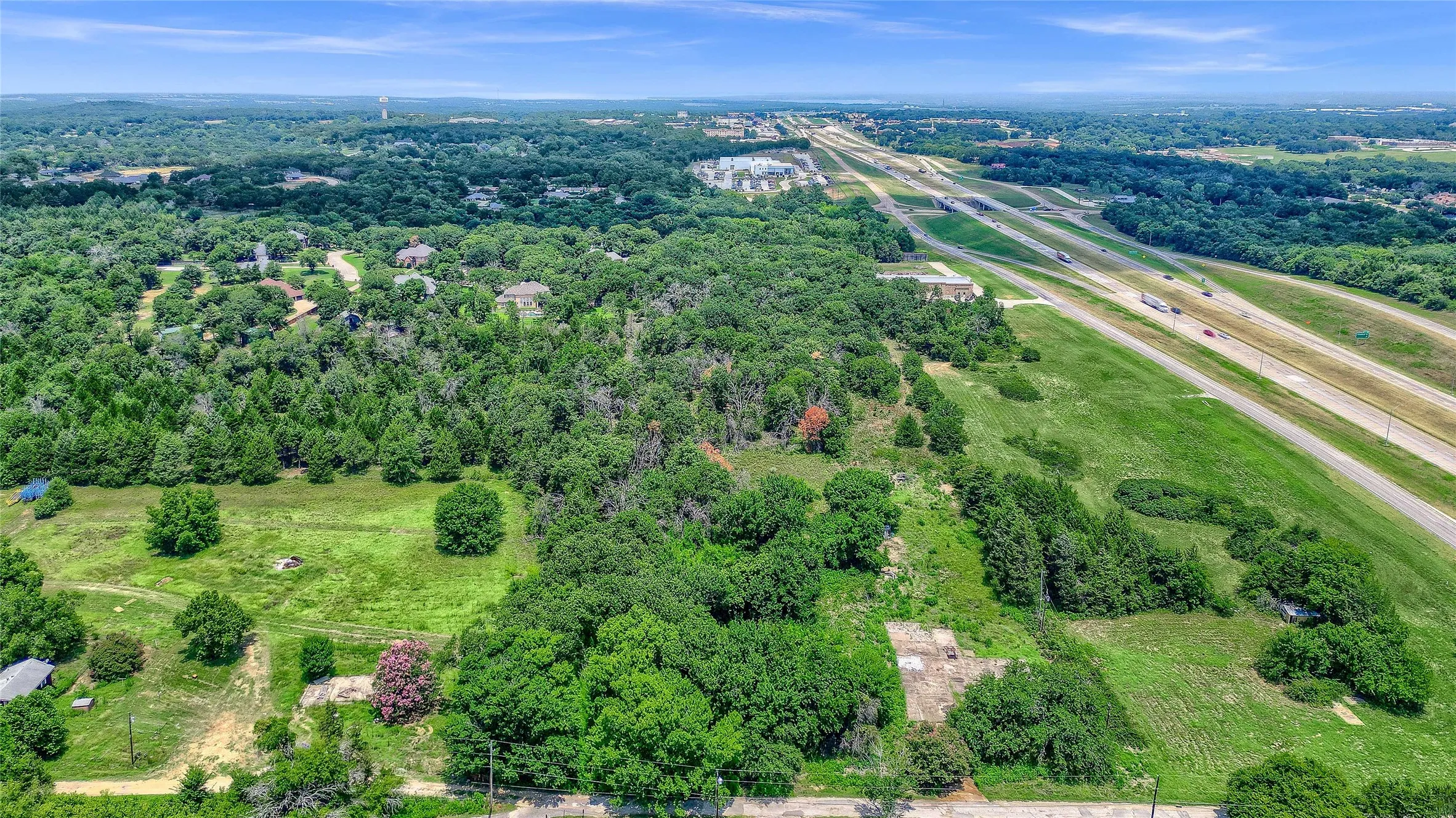 Expansive land parcel featuring dense tree coverage, open grassy areas, and a multi-lane highway