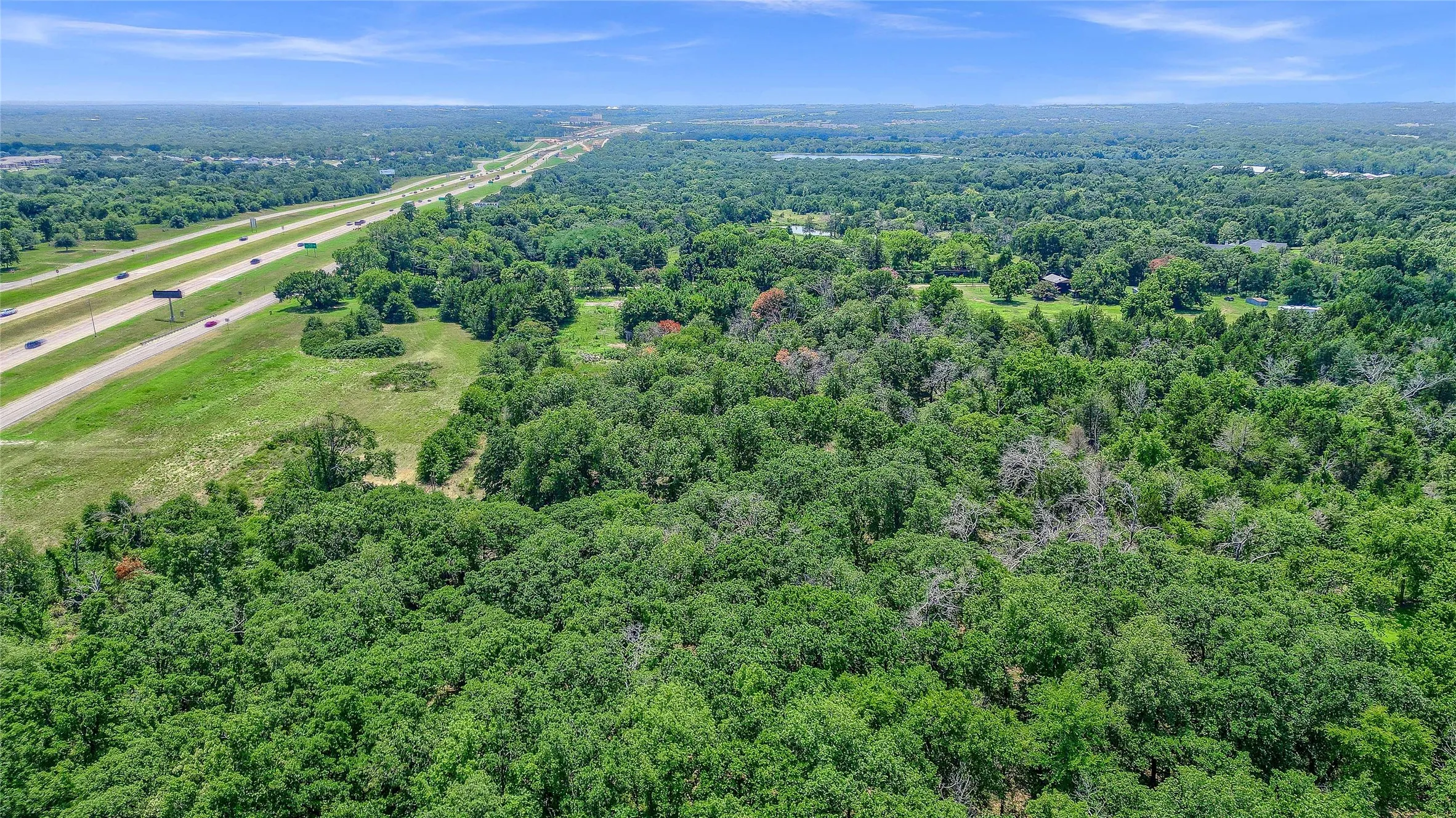 Expansive wooded terrain with highway frontage and distant water body