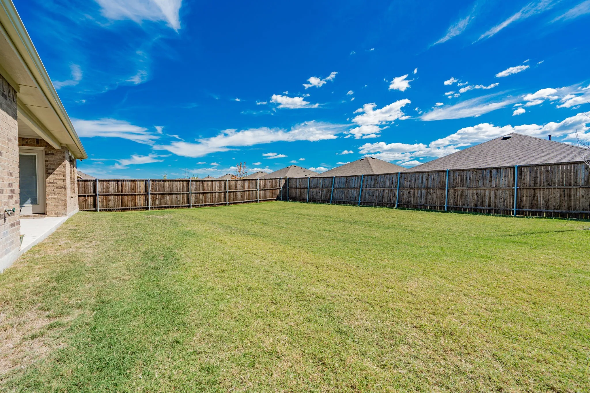 Expansive backyard with a manicured lawn, full privacy fencing, and a concrete patio