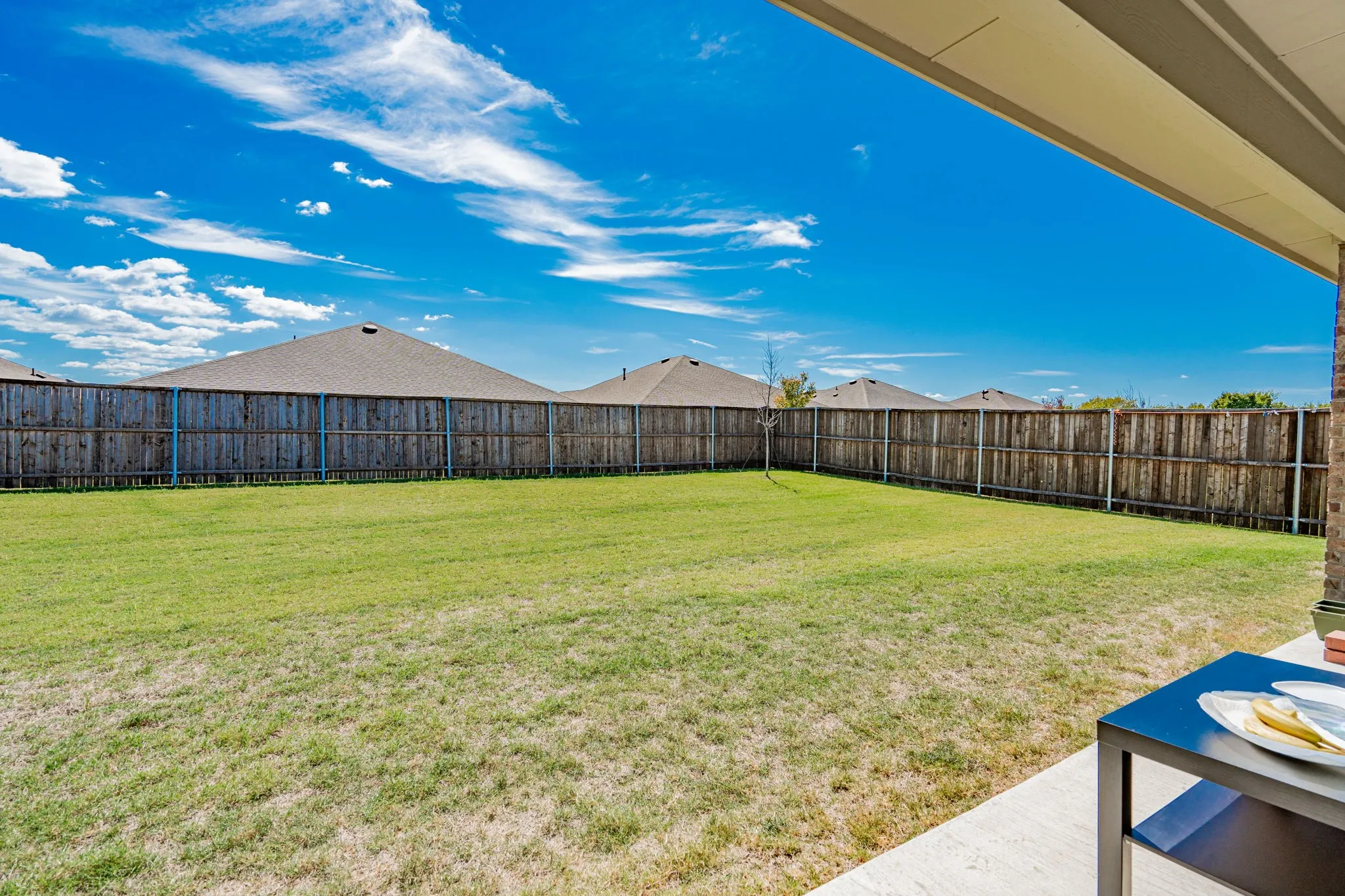 Expansive backyard featuring a manicured lawn, a wood fence, and a concrete patio