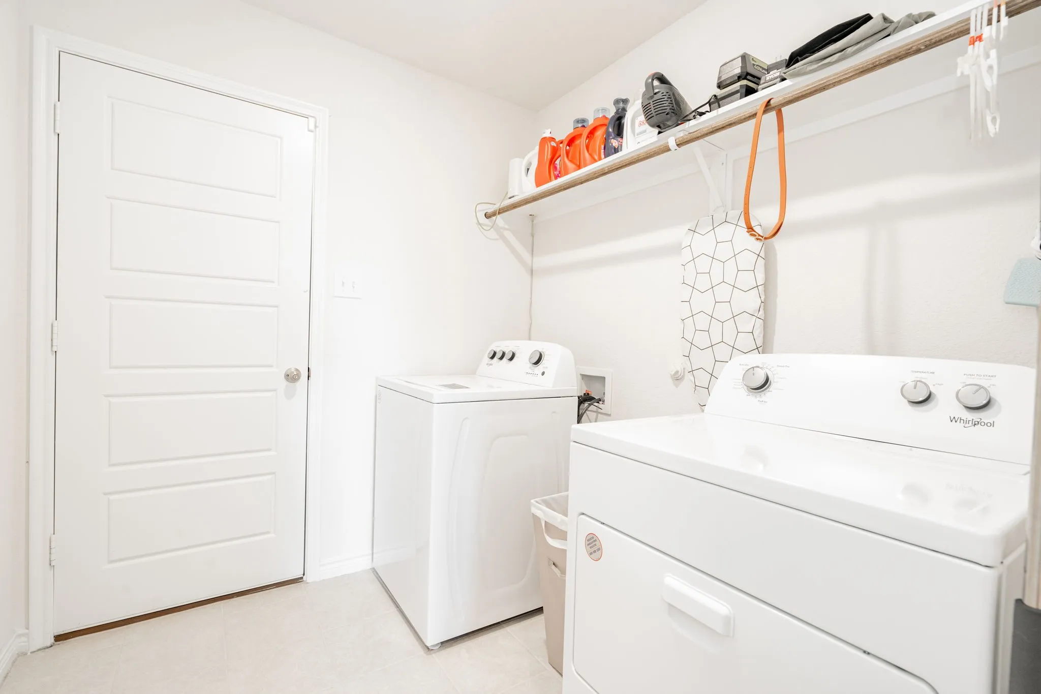 Laundry area featuring a top-load washing machine, front-load dryer, and wall-mounted shelving with a hanging rod