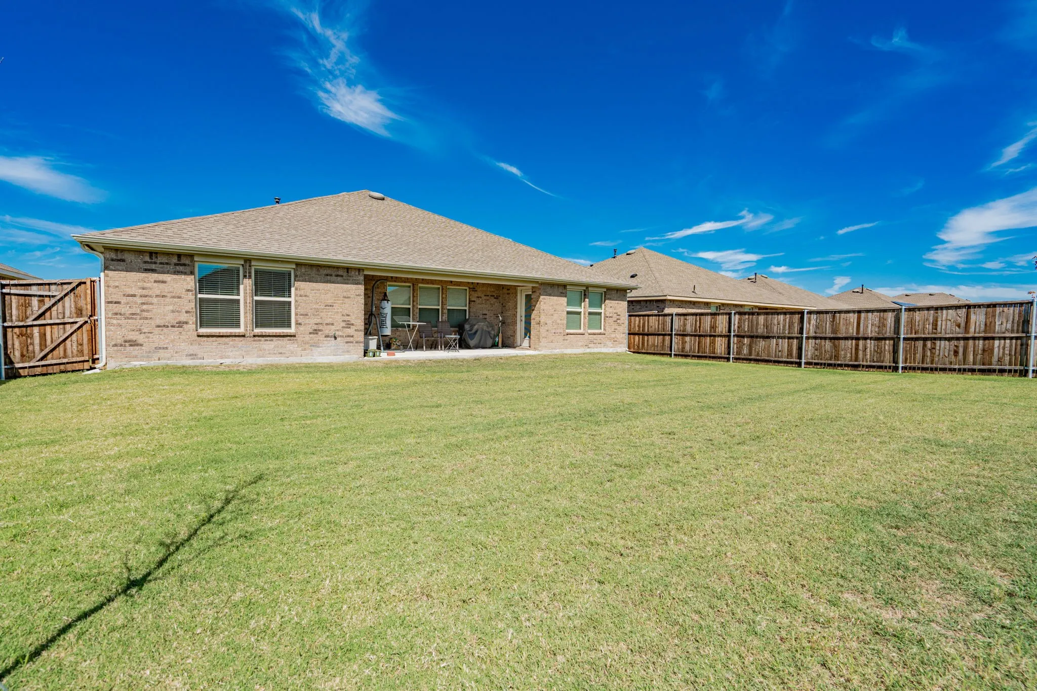 Expansive backyard featuring a manicured lawn, full privacy fencing, brick exterior, and a concrete patio