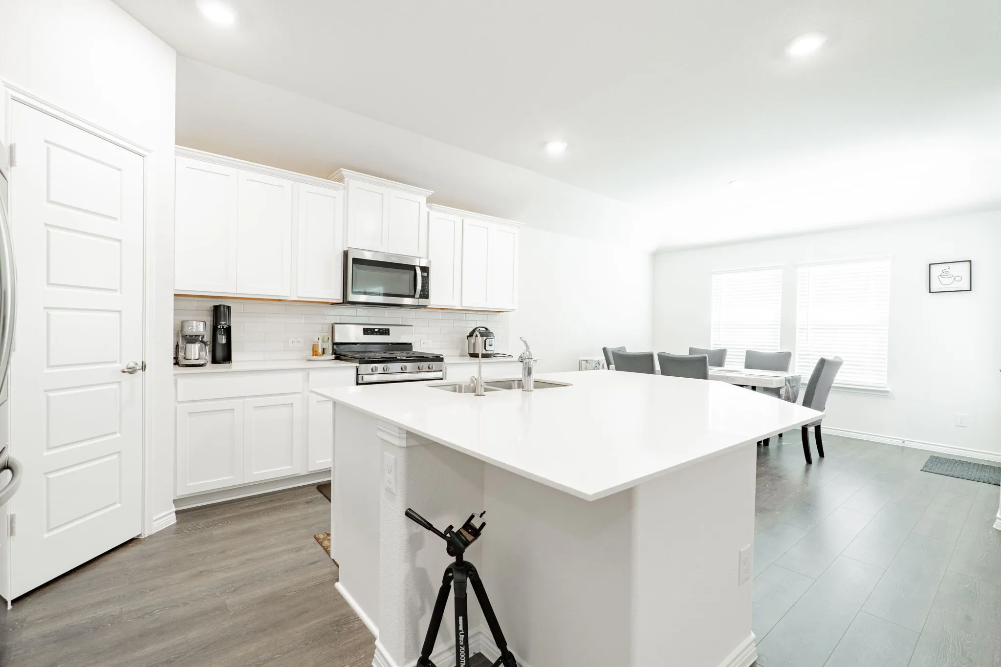 Modern kitchen and dining area featuring white cabinetry, stainless steel appliances, quartz waterfall island countertop, wood-finish flooring, and recessed ceiling lighting