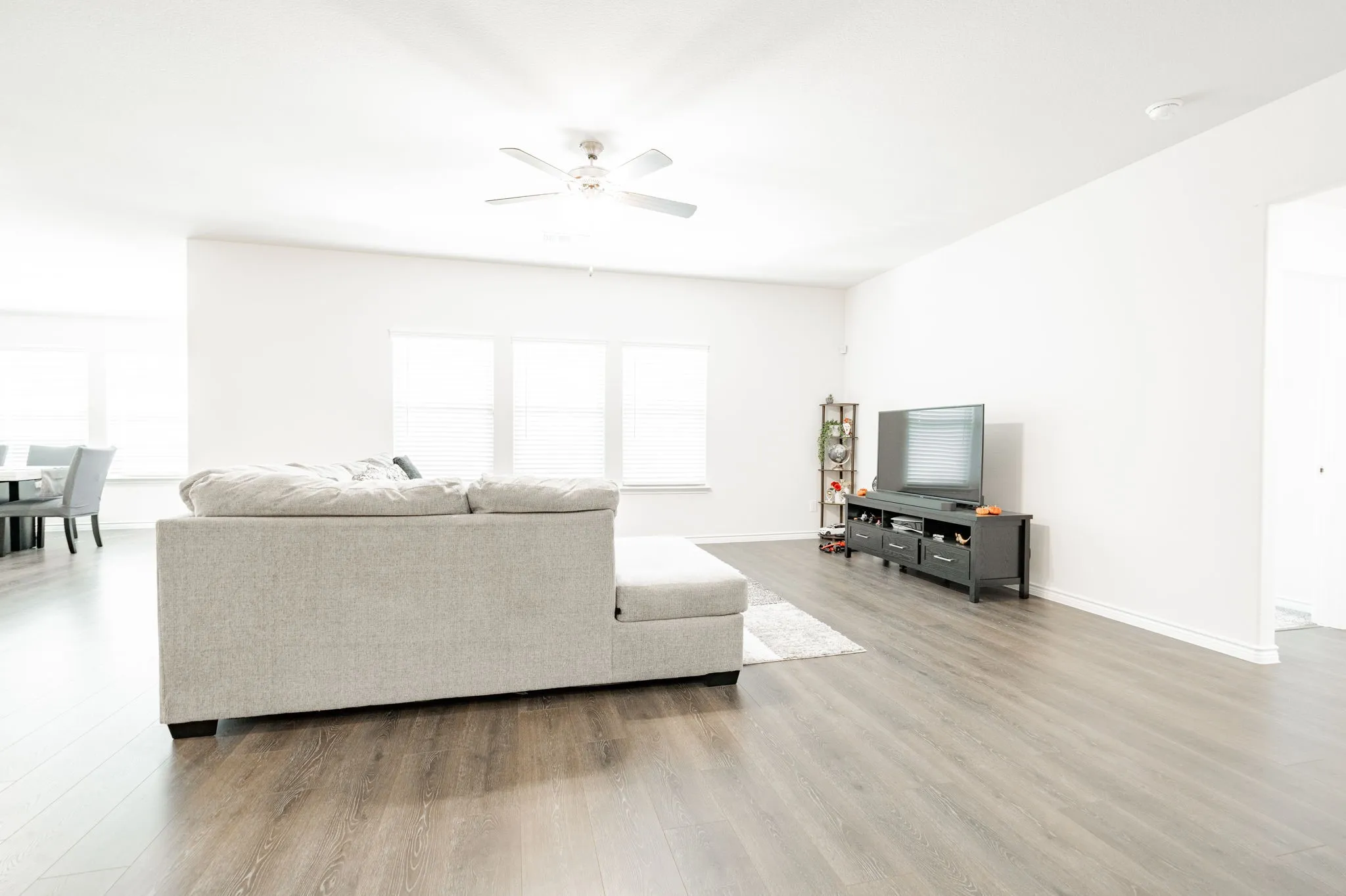 Wood-finish flooring throughout, white walls, multiple windows with blinds, and ceiling fan