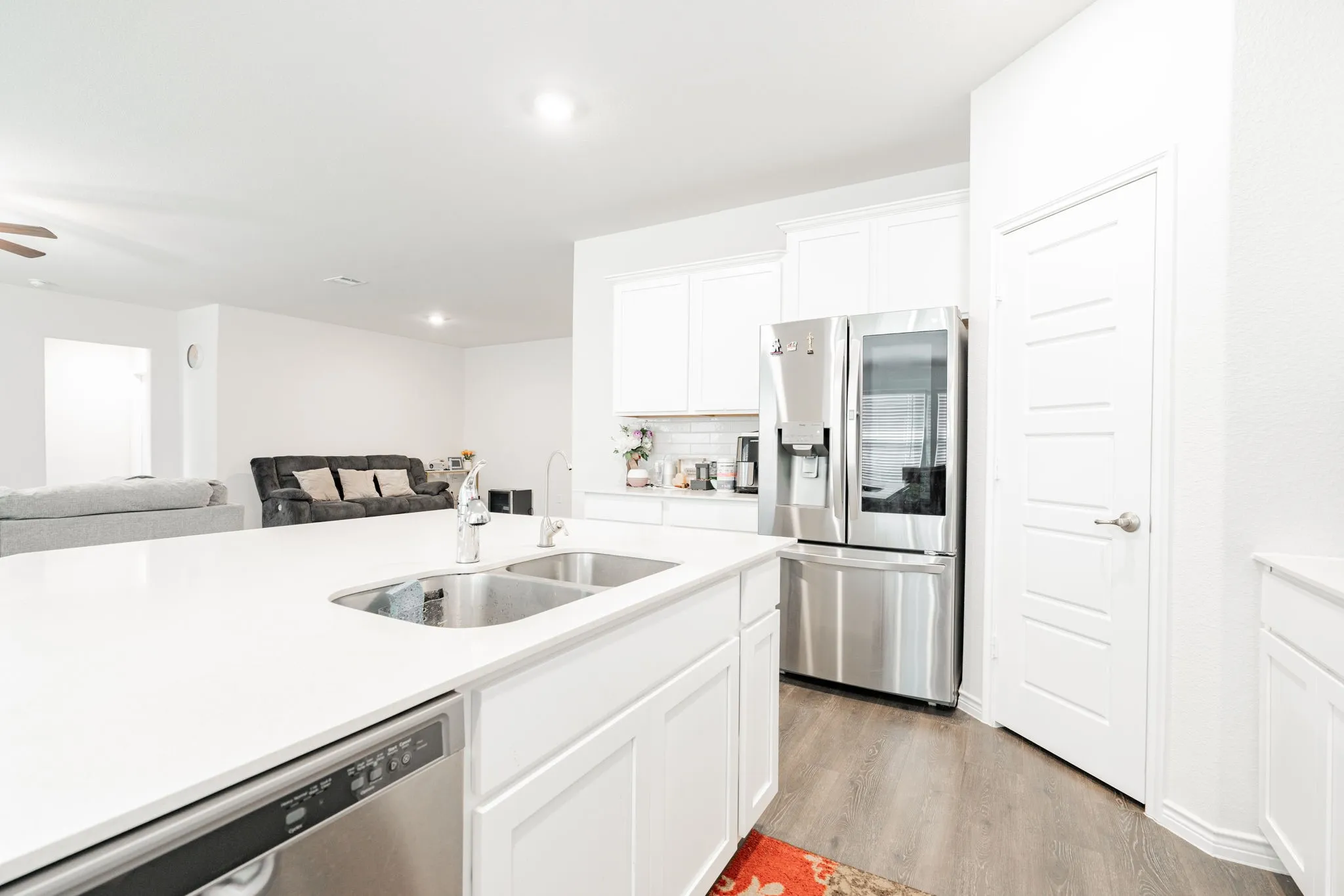 Kitchen featuring an expansive island with a dual basin sink, stainless steel appliances, white cabinetry, and wood-finish flooring