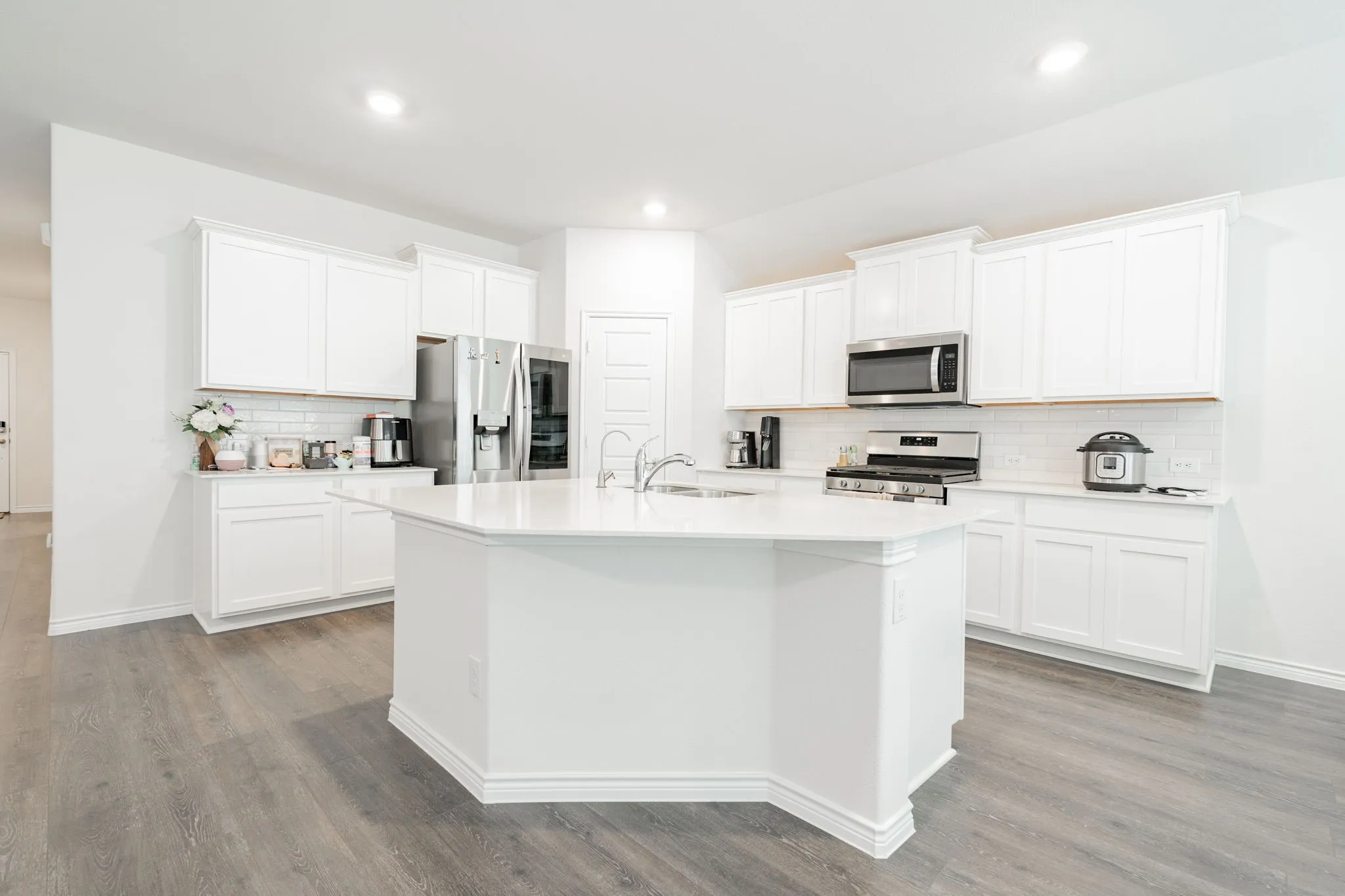 Kitchen featuring an expansive white island, white cabinetry, stainless steel appliances, white subway tile backsplash, and wood-finish flooring