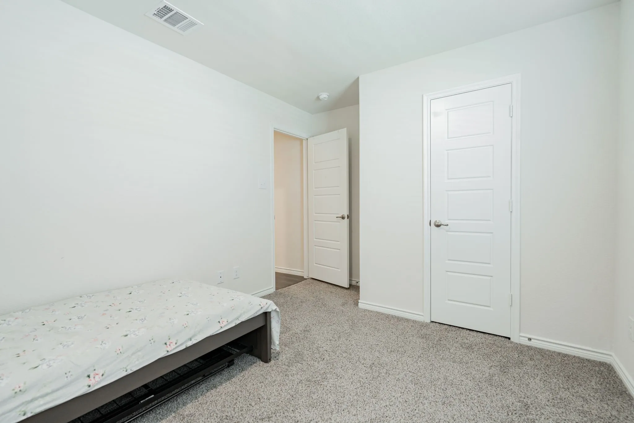 Bright bedroom with neutral carpeting, two closet doors with horizontal paneling, and clean white walls throughout
