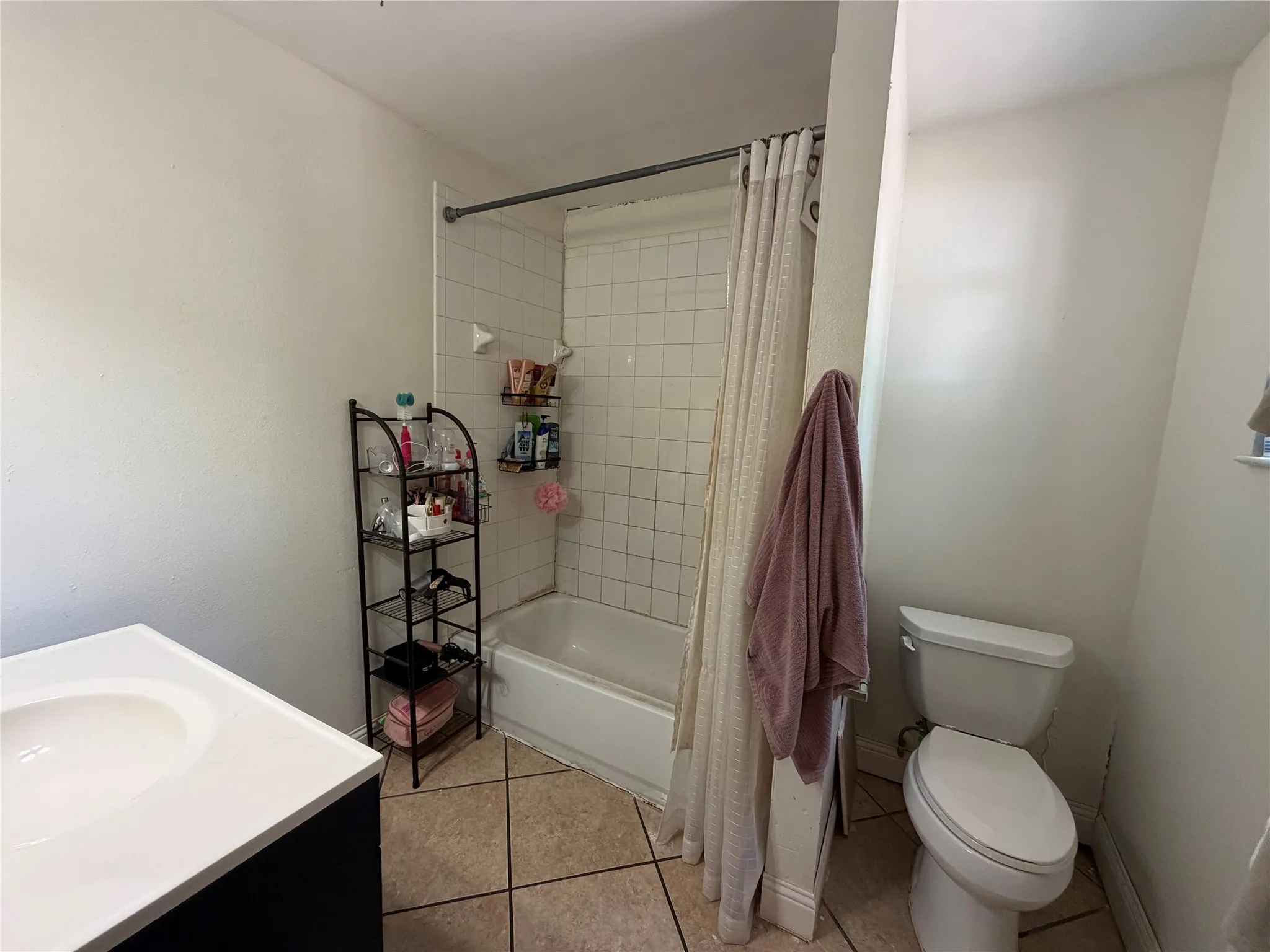 White ceramic tile shower surround with a built-in tub, white vanity with an integrated sink, and light-toned tile flooring