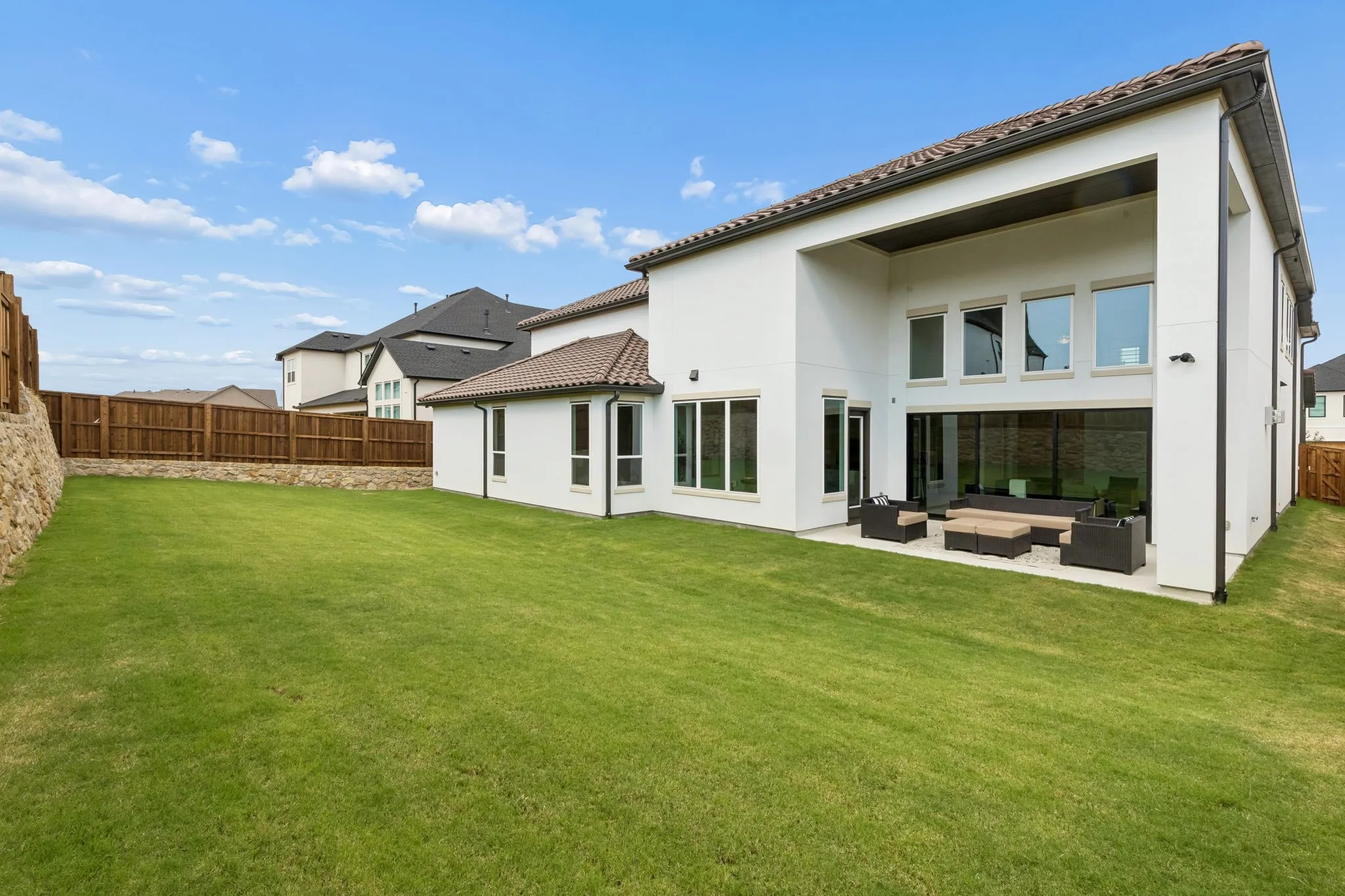 Expansive rear yard with a manicured lawn, stucco exterior, tiled roof, and a covered patio