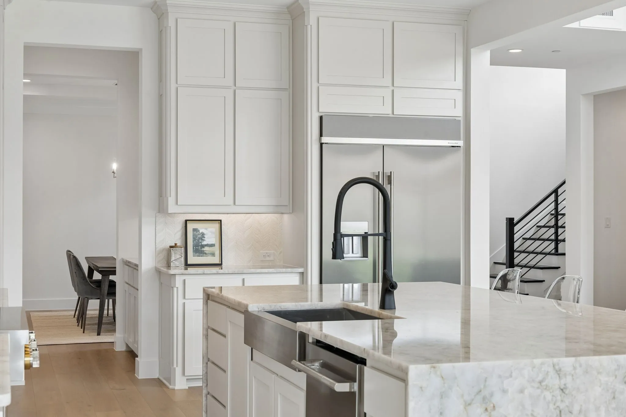 White shaker cabinetry, stainless steel appliances, light-toned stone countertops, matte black faucet, and wood-finish flooring