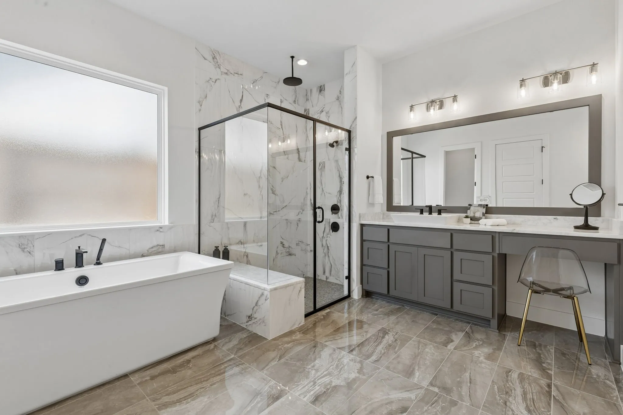 Freestanding soaking tub with matte black fixtures, glass-enclosed shower with full-height tile surround, dual vanity with undermount sinks, and large framed mirror