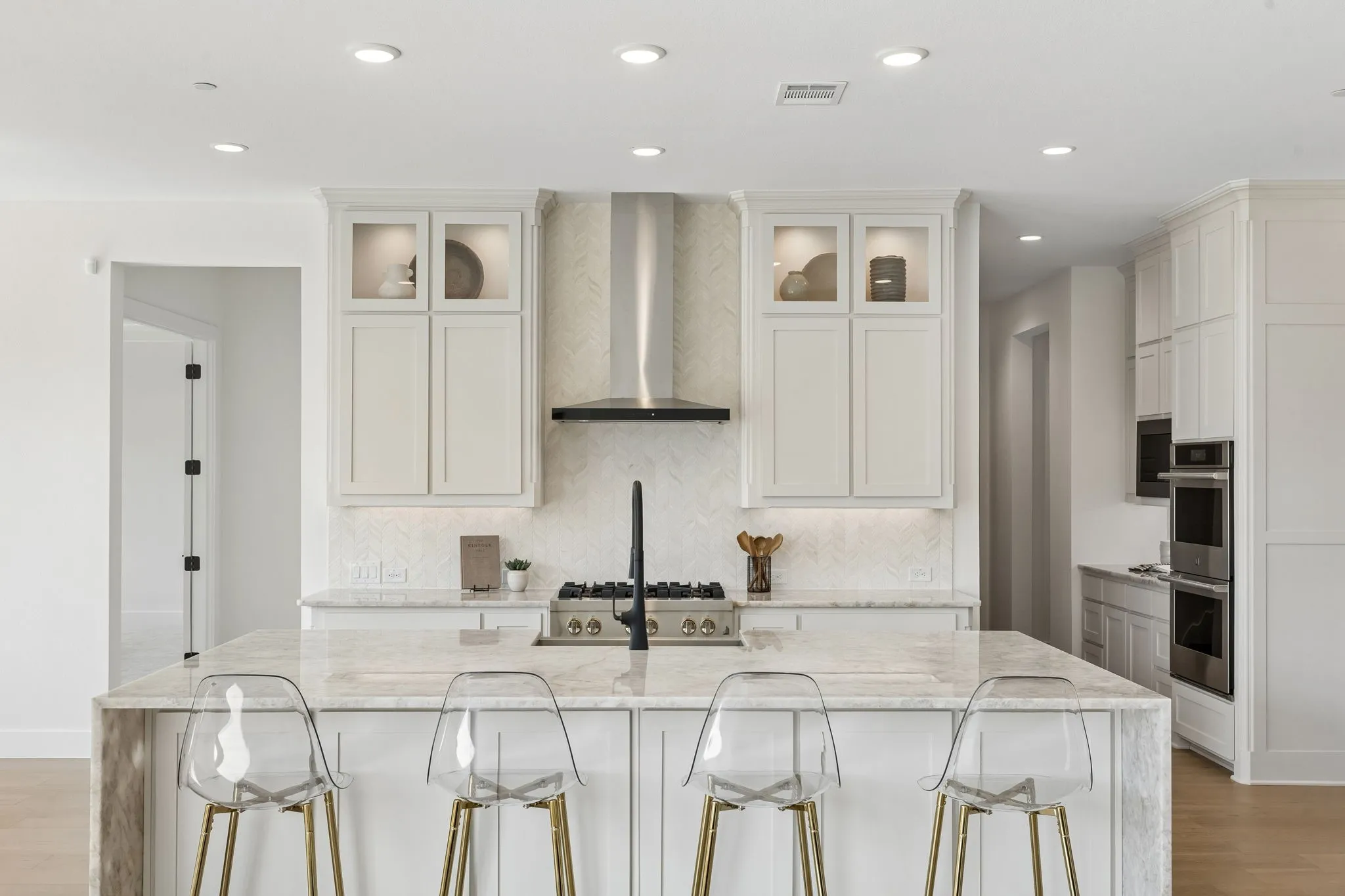 Spacious kitchen featuring a large island, stainless steel appliances, recessed lighting, and ample white cabinetry with glass-front accents