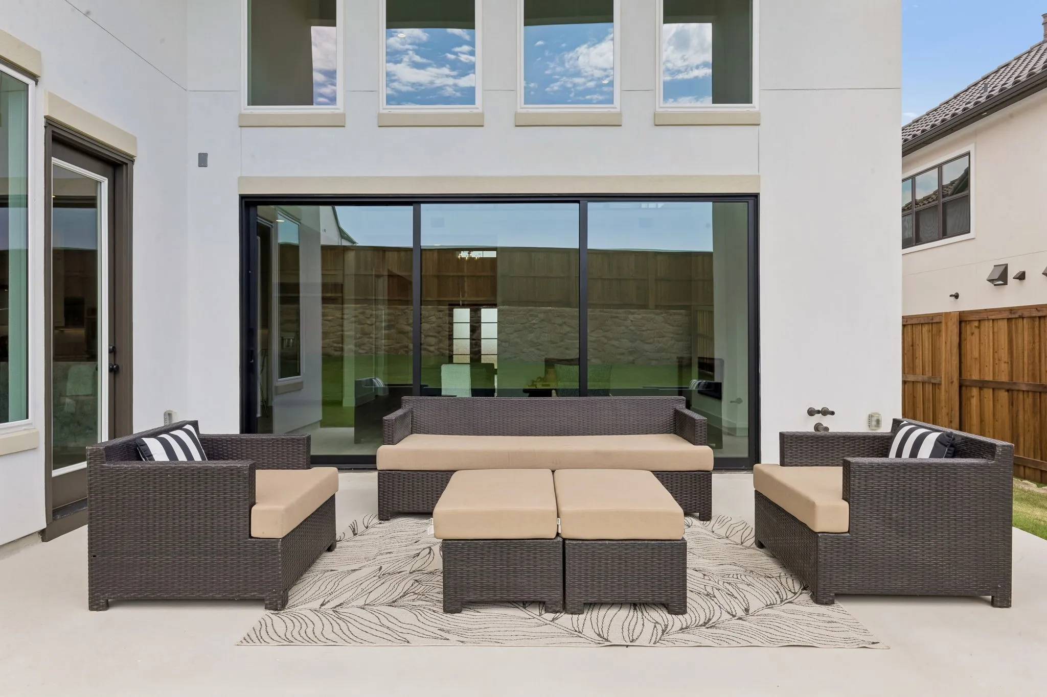 White stucco exterior with multiple windows, large sliding glass doors, and a concrete patio