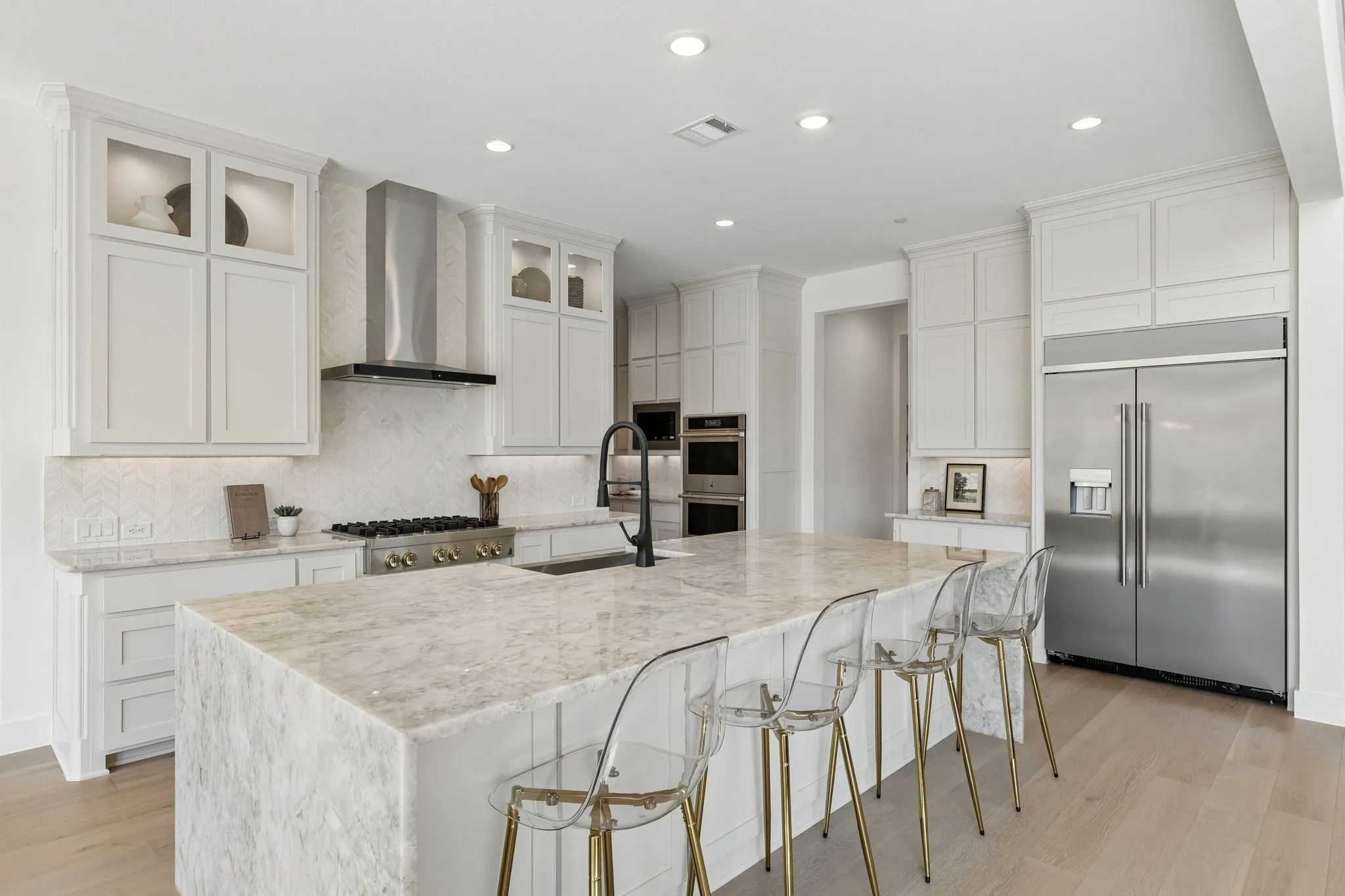 Expansive kitchen island with a stone countertop, white cabinetry, integrated stainless steel appliances, and wood-finish flooring