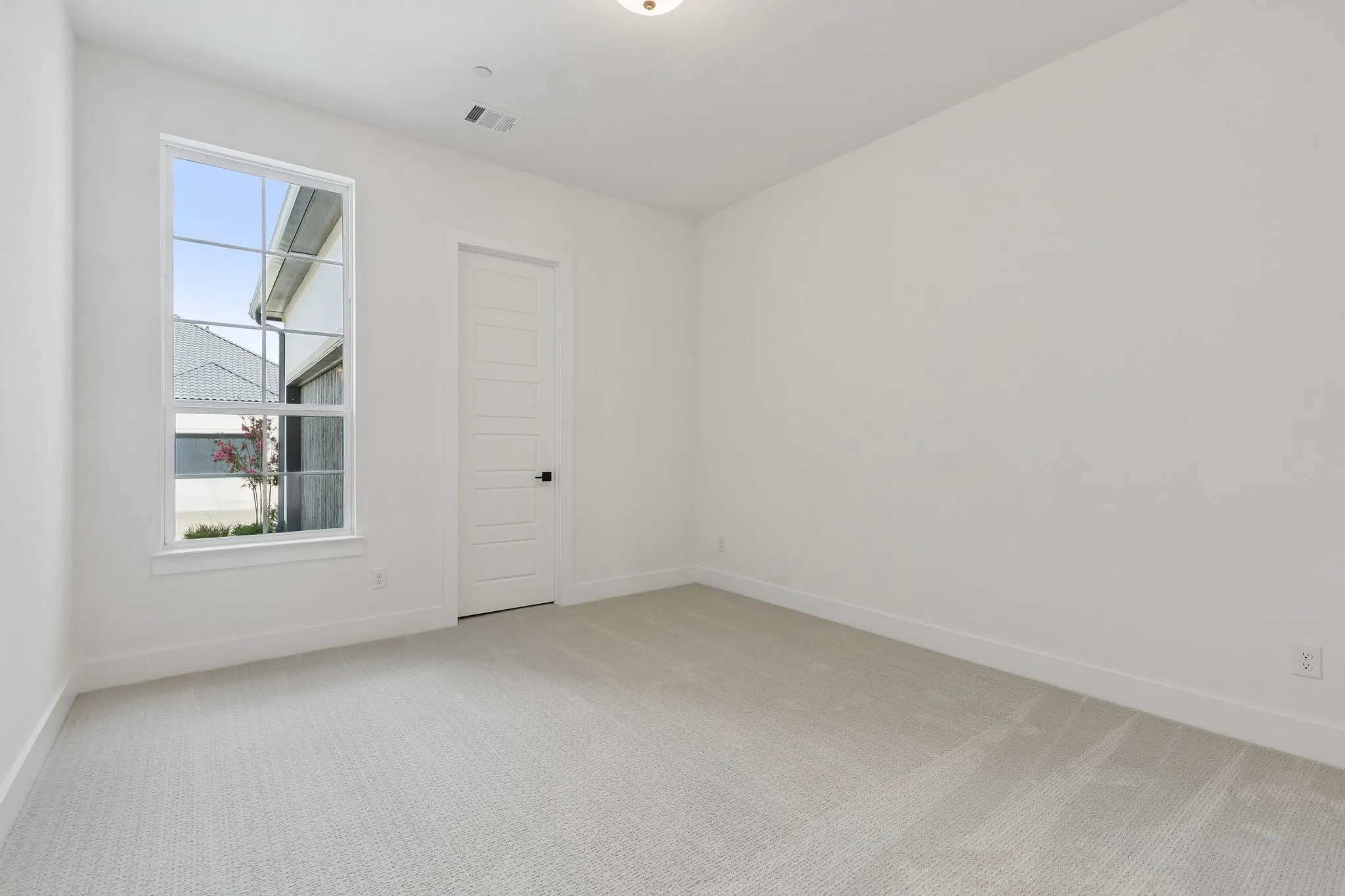Secondary downstairs bedroom, light-toned carpeting, crisp white walls, and a multi-pane window with white trim