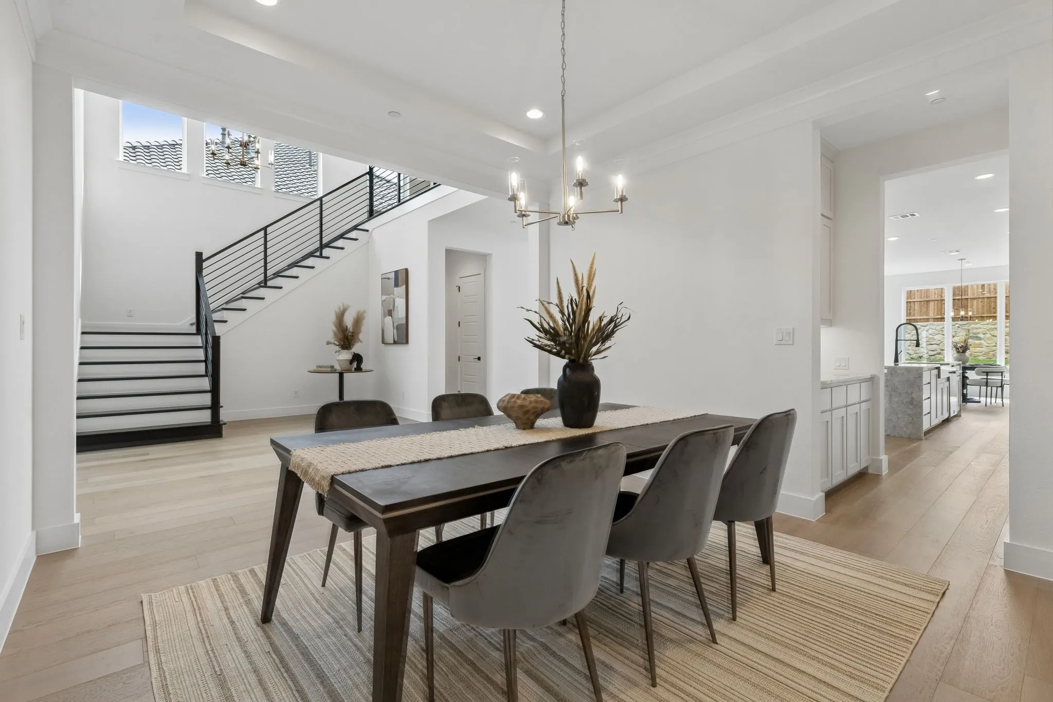 Light wood-finish flooring, a modern chandelier, and a black metal staircase railing