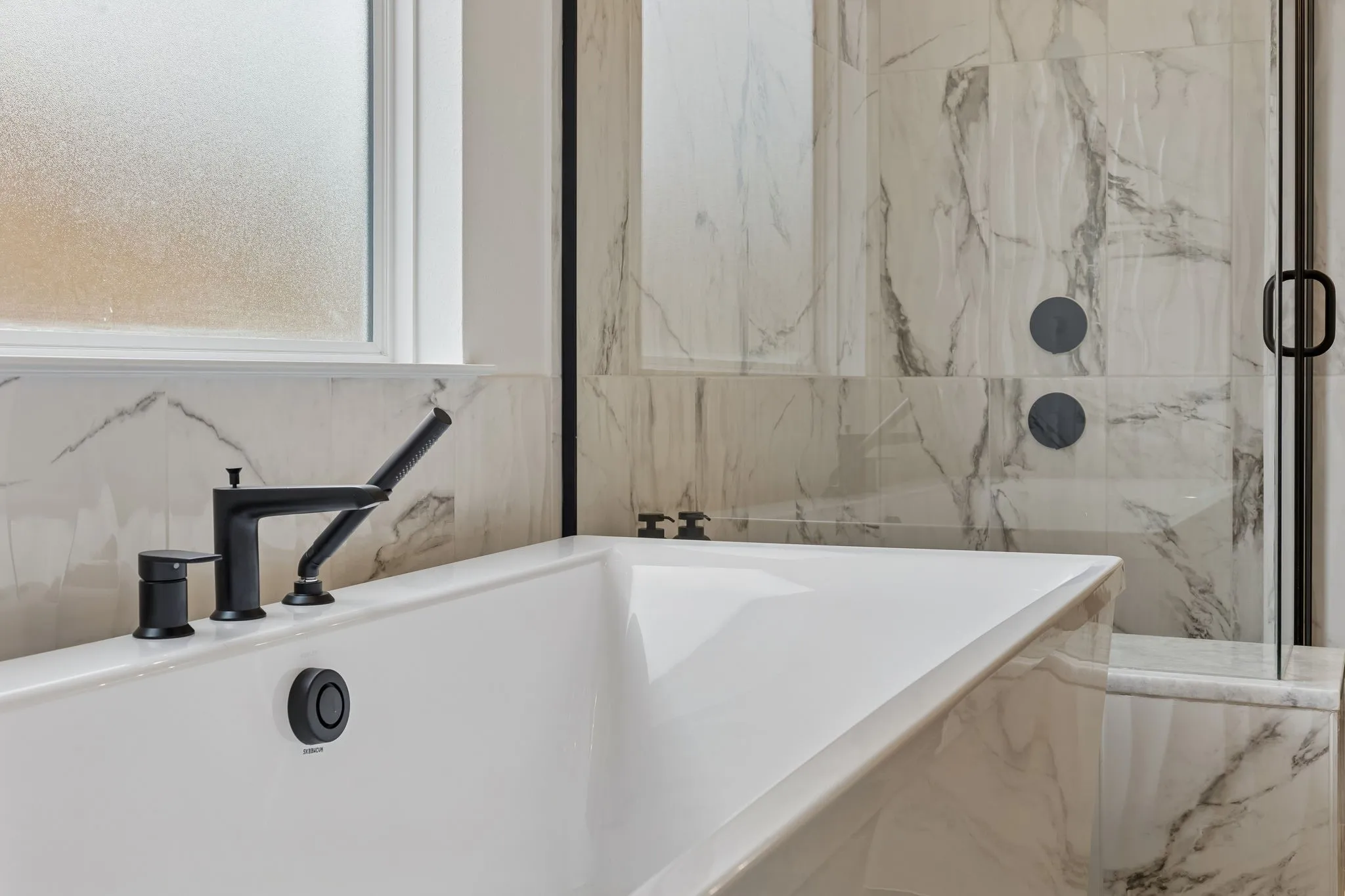 Built-in soaking tub with matte black fixtures, surrounded by large format tile with natural stone veining, and a frameless glass shower enclosure