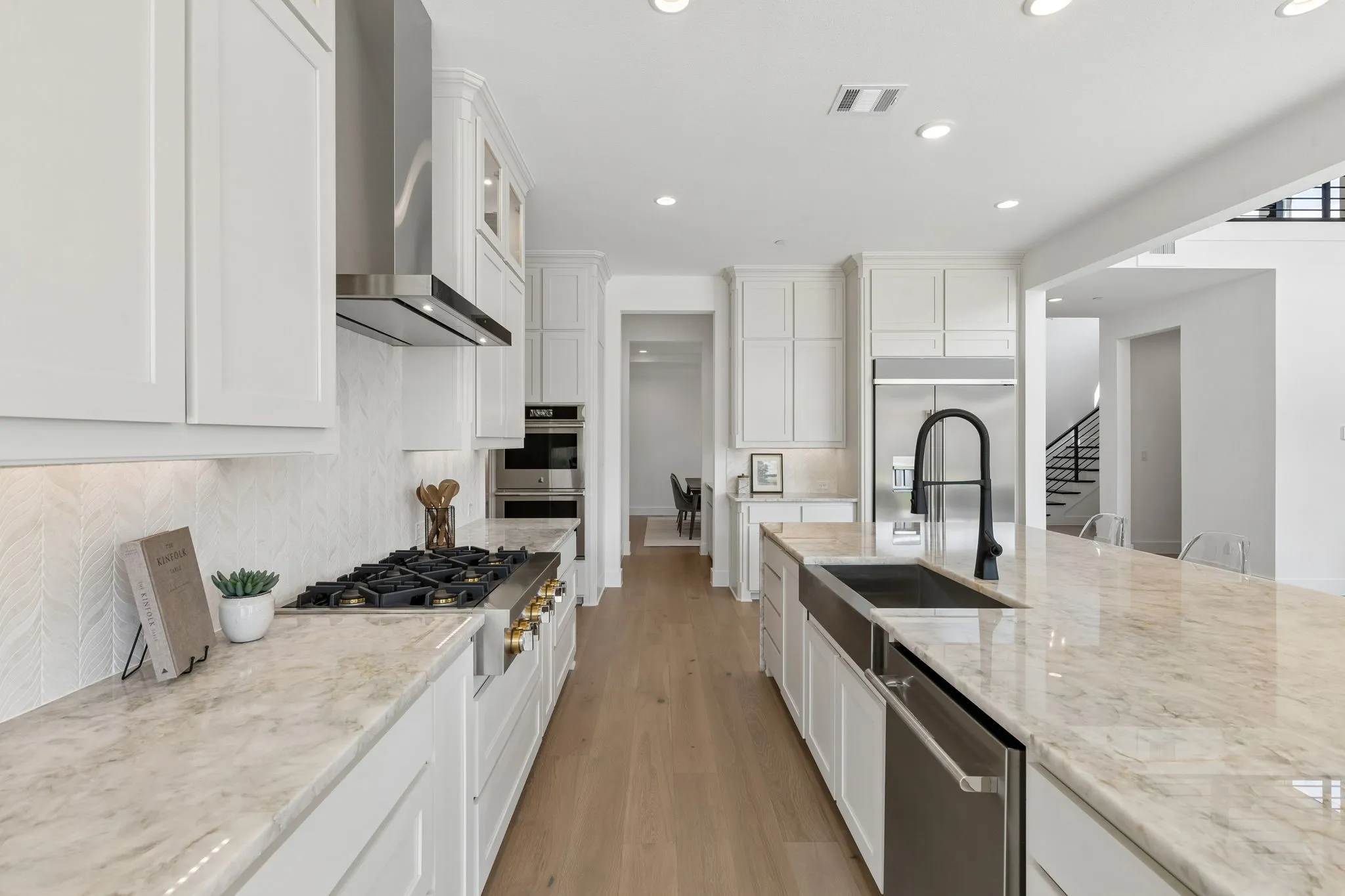 Gourmet kitchen featuring a gas range, stainless steel appliances, a large island with a farmhouse sink, stone countertops, and light wood-finish flooring