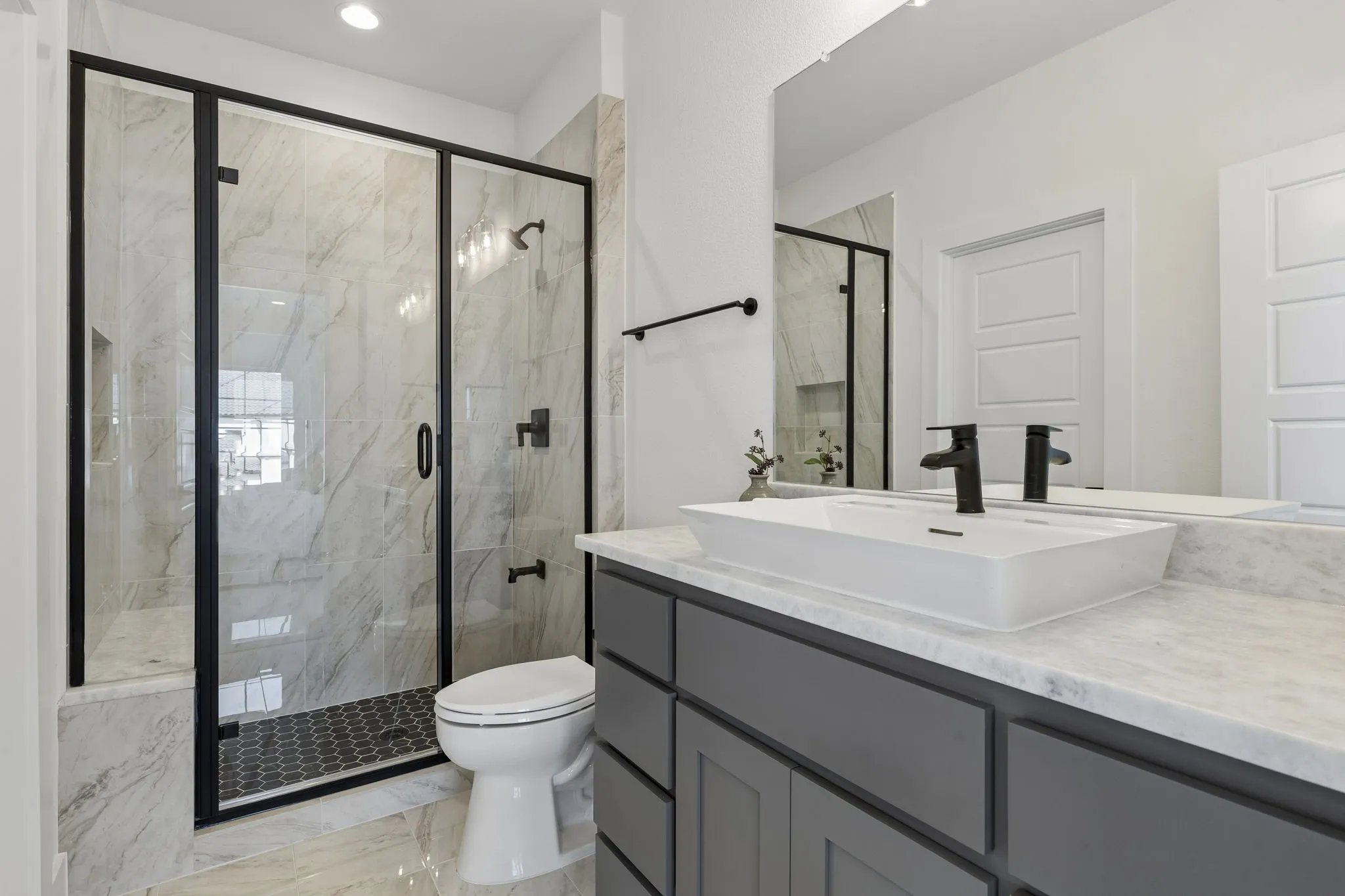 Curated bathroom featuring a glass-enclosed shower with matte black fixtures, a vessel sink, a stone-finish countertop, and a gray vanity with panel-front cabinetry