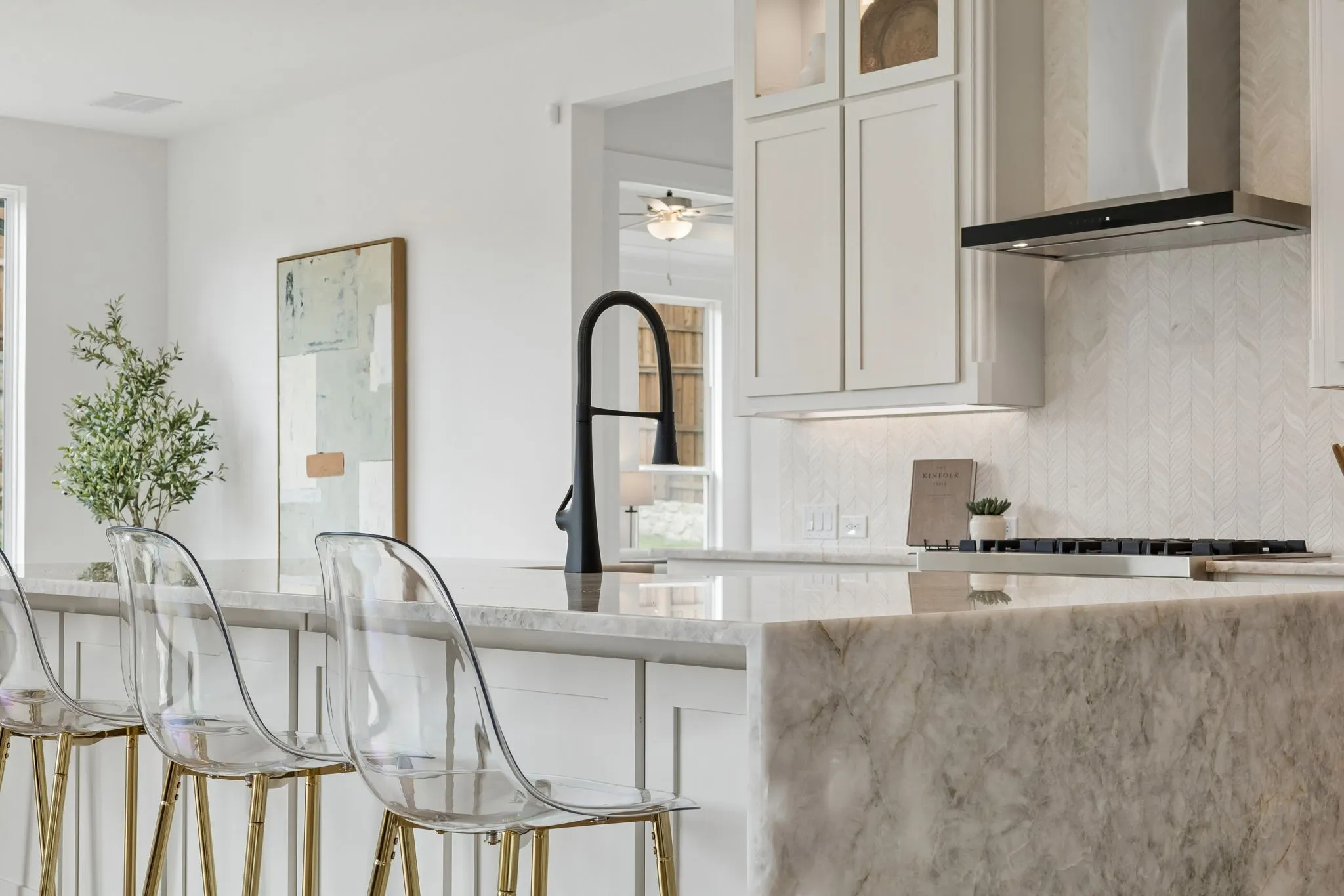 Kitchen island featuring a waterfall countertop, integrated cooktop, white shaker-style cabinetry, and a black gooseneck faucet
