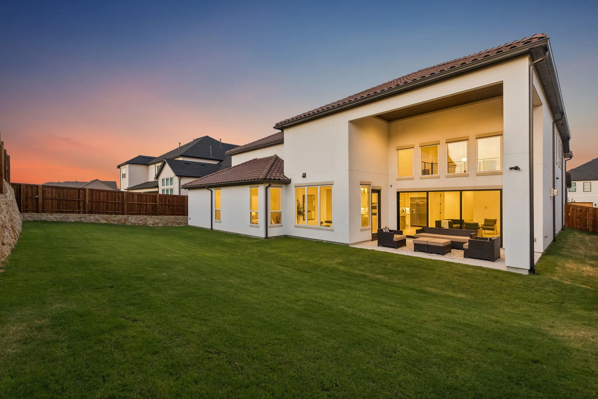 Expansive manicured lawn with a stone retaining wall, private wood fence, and covered patio featuring a built-in fire pit