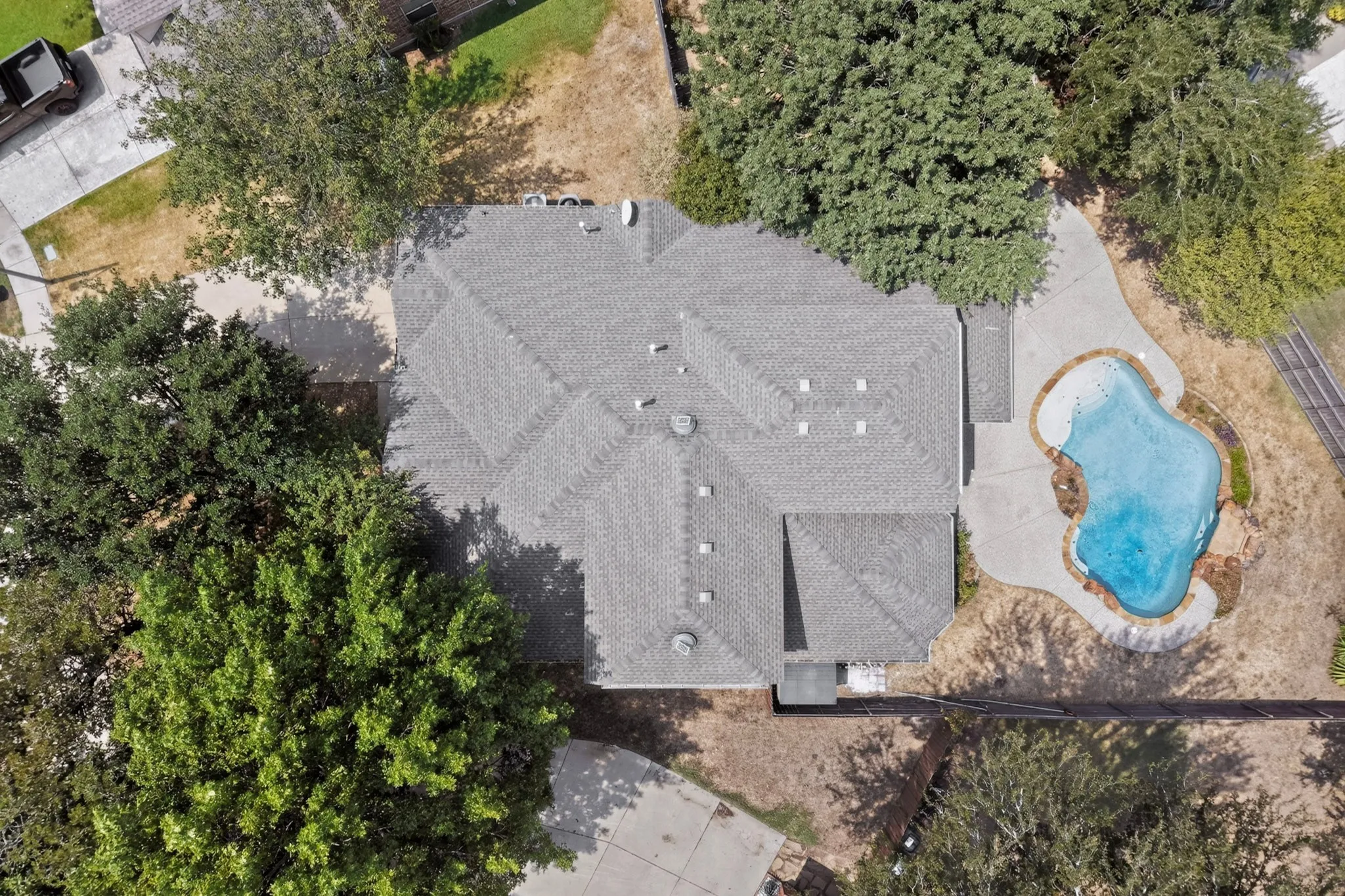 Asphalt shingle roofing, mature trees, and a free-form swimming pool with a concrete surround