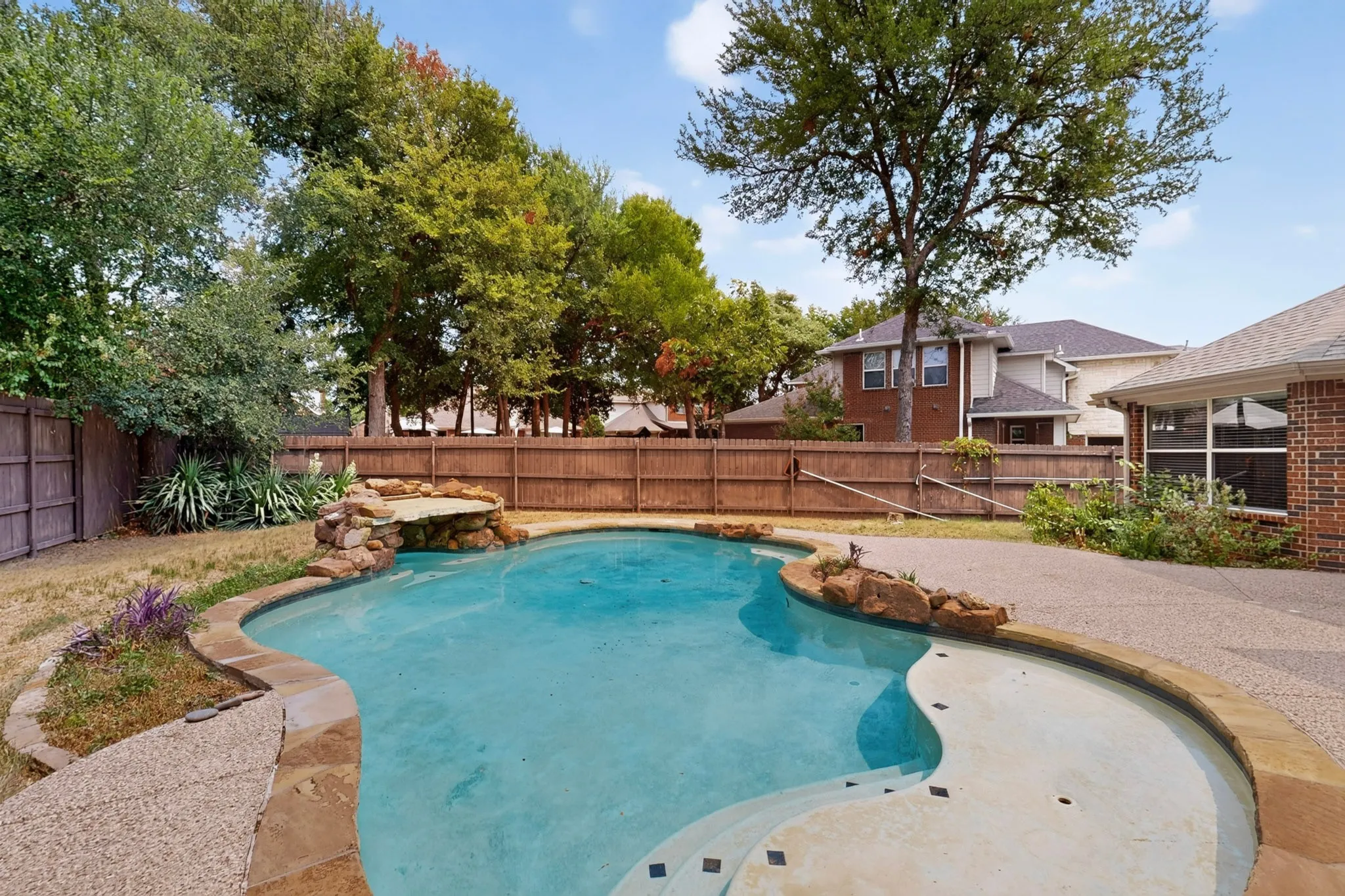 Freeform swimming pool with rock waterfall feature, integrated steps, and textured concrete decking