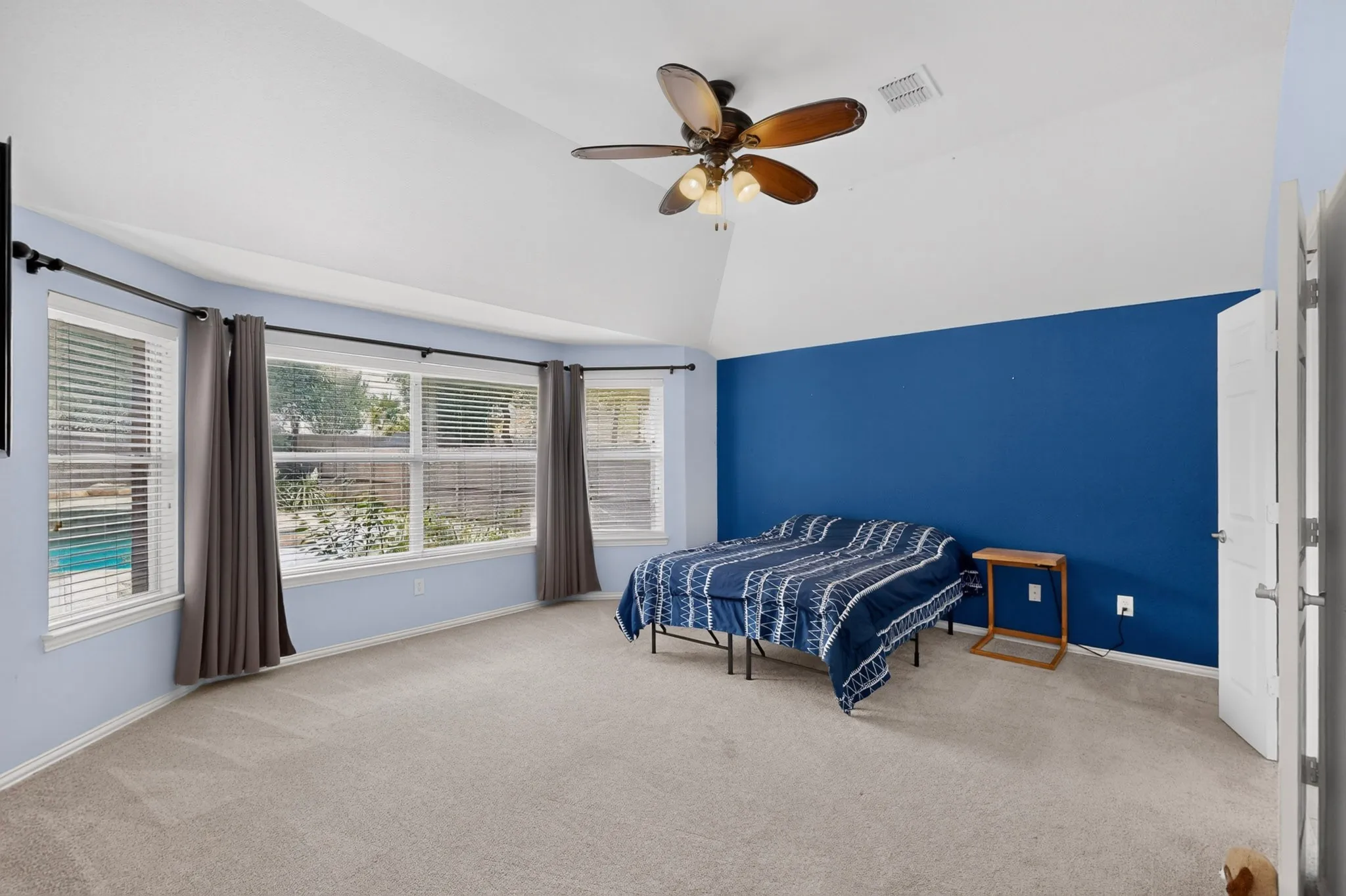 Vaulted ceiling with ceiling fan, large windows with horizontal blinds, neutral carpet flooring, and a solid door