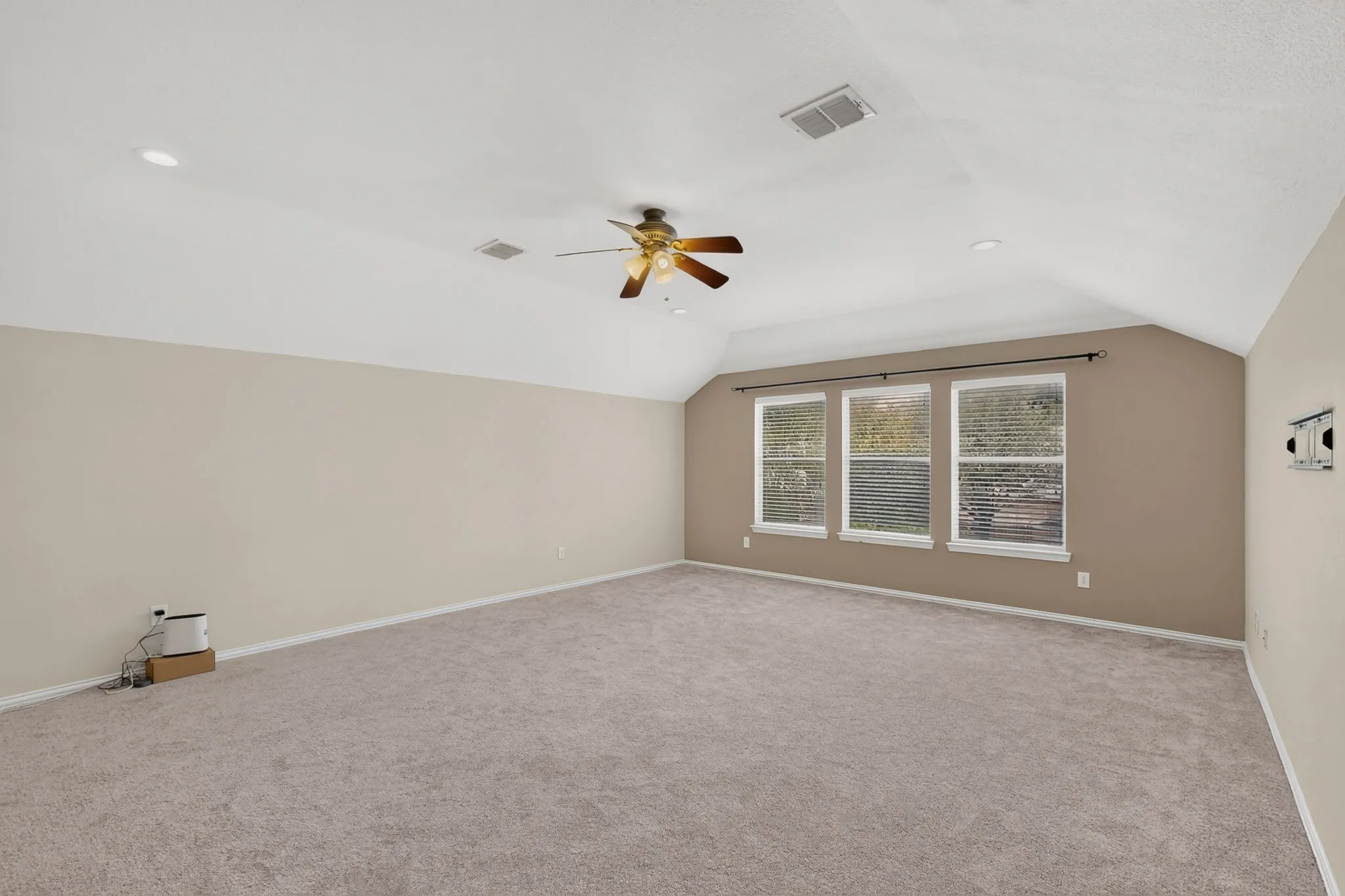 Spacious room featuring vaulted ceilings, recessed lighting, a ceiling fan, three windows, and carpet flooring