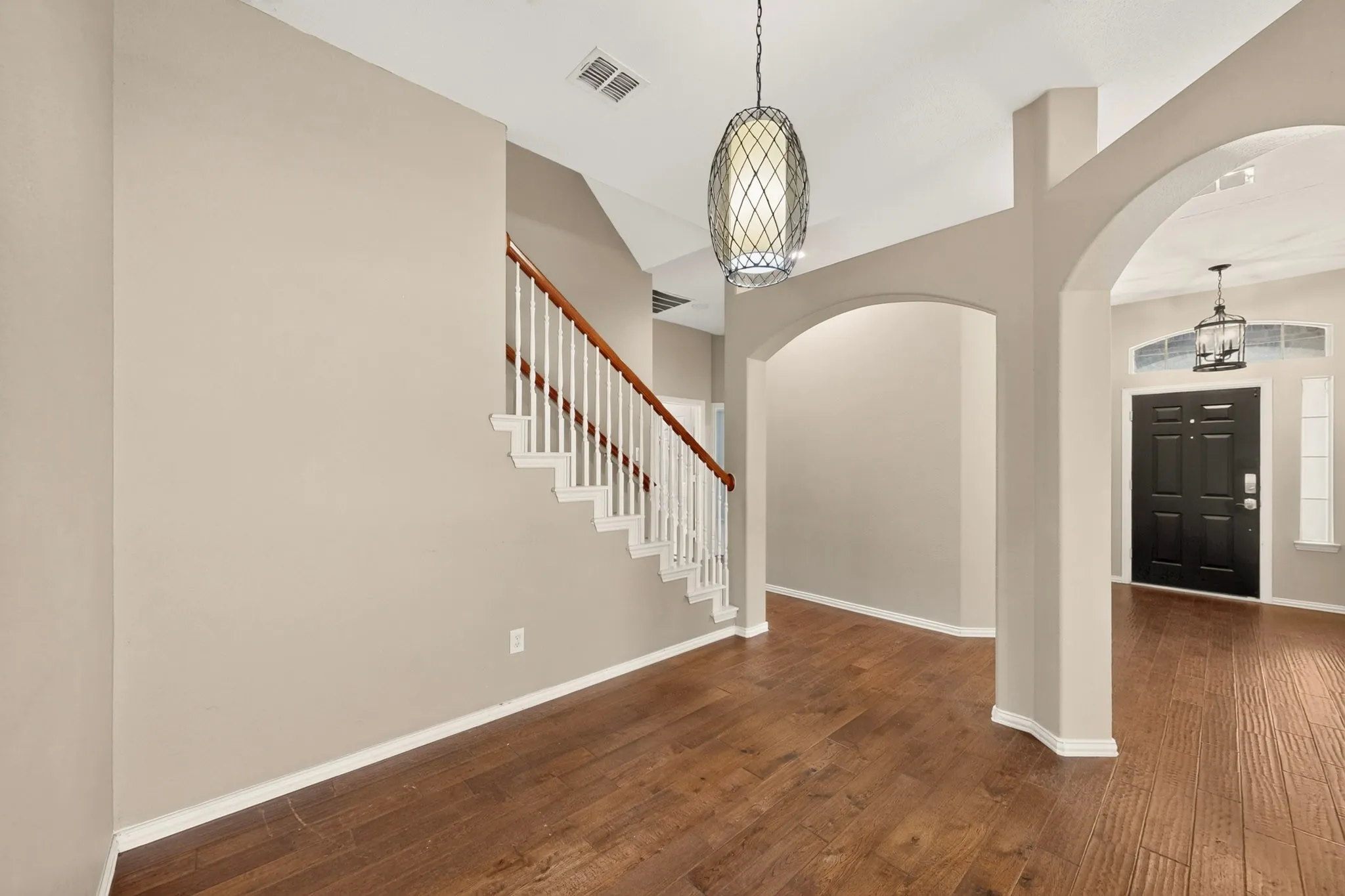 Wood-finish flooring, vaulted ceiling, staircase with white risers and wood handrail, arched doorways, and a dark paneled entry door
