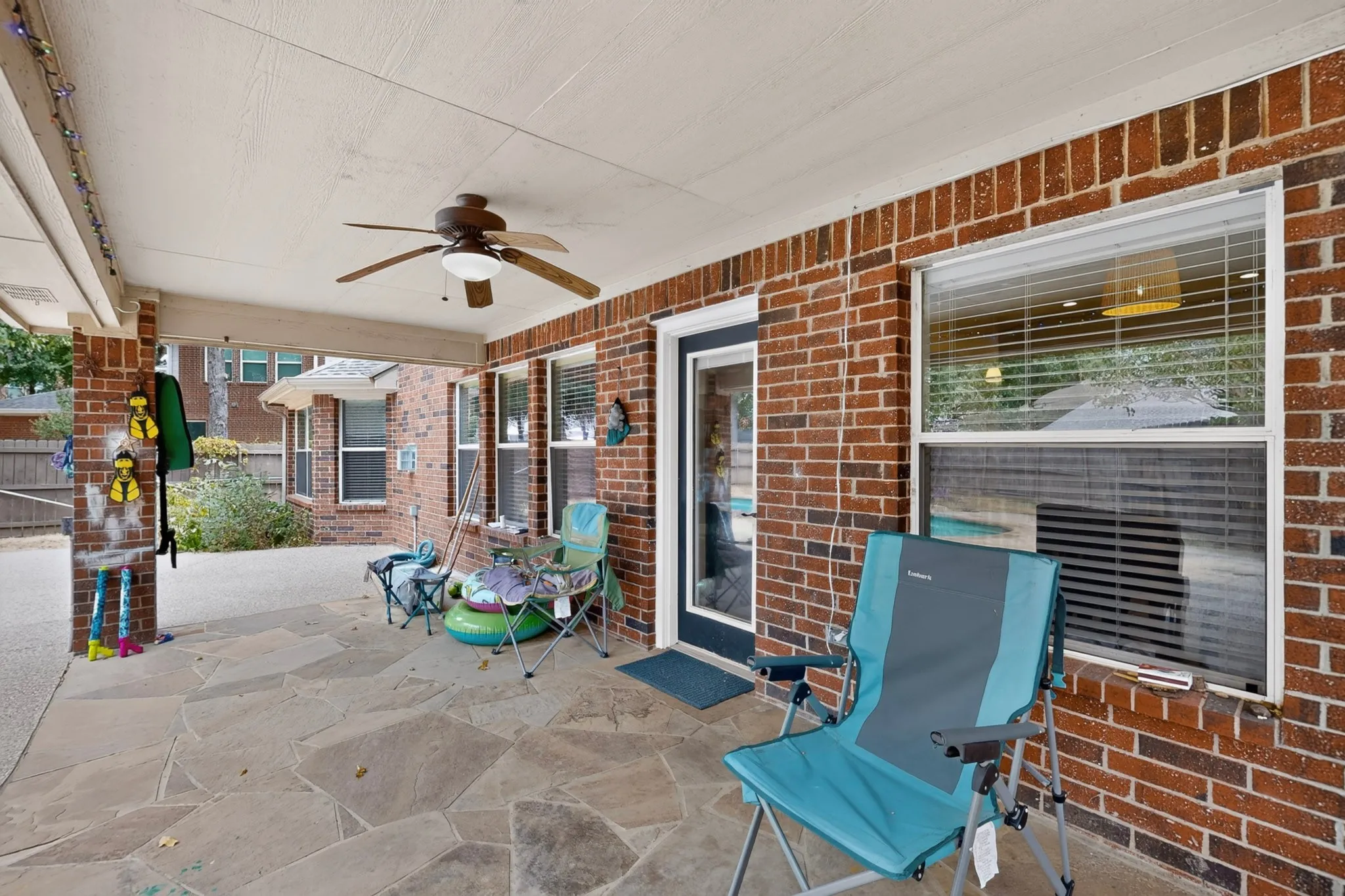 Covered outdoor patio featuring flagstone flooring, brick exterior, and a ceiling fan