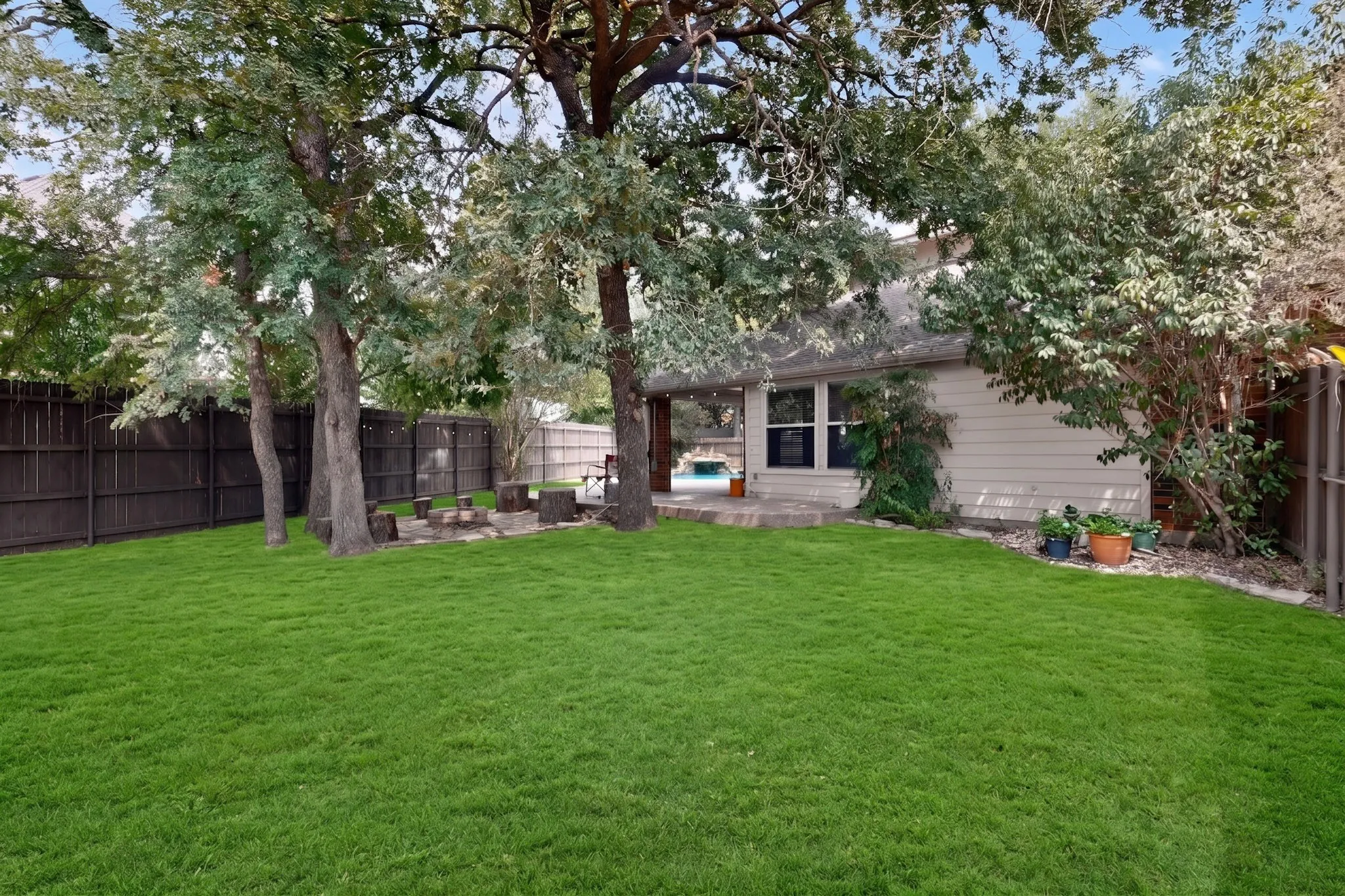 Spacious backyard featuring a manicured lawn, established trees, and perimeter fencing