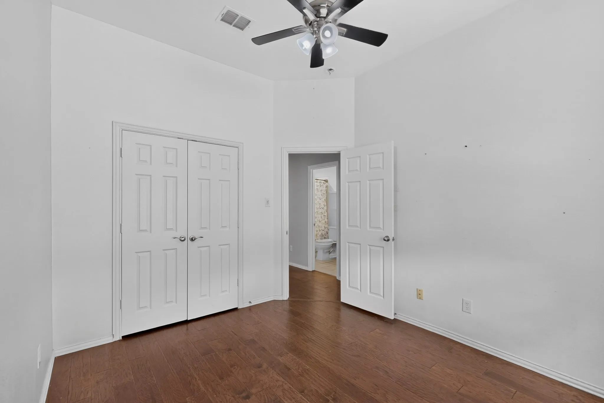 Wood-finish flooring, vaulted ceiling, ceiling fan with integrated lighting, paneled doors, and an en-suite bathroom