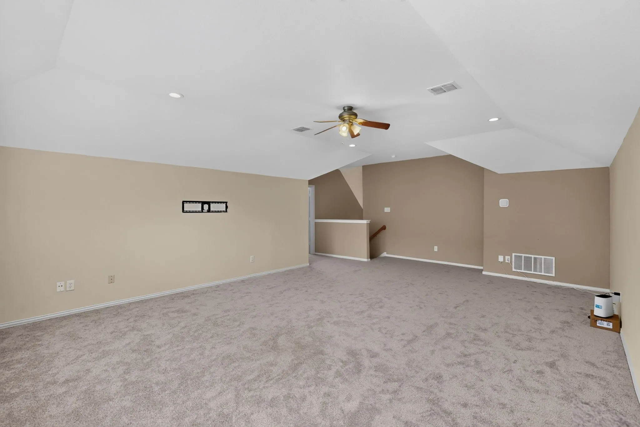 Expansive carpeted area with recessed lighting, a ceiling fan, and a wall-mounted bracket