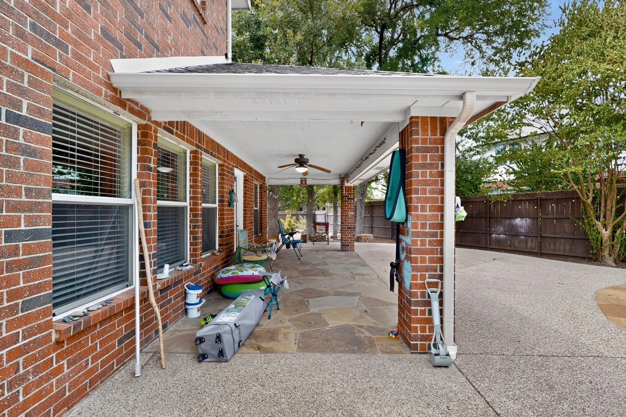 Covered patio featuring brick pillars, flagstone flooring, and a ceiling fan