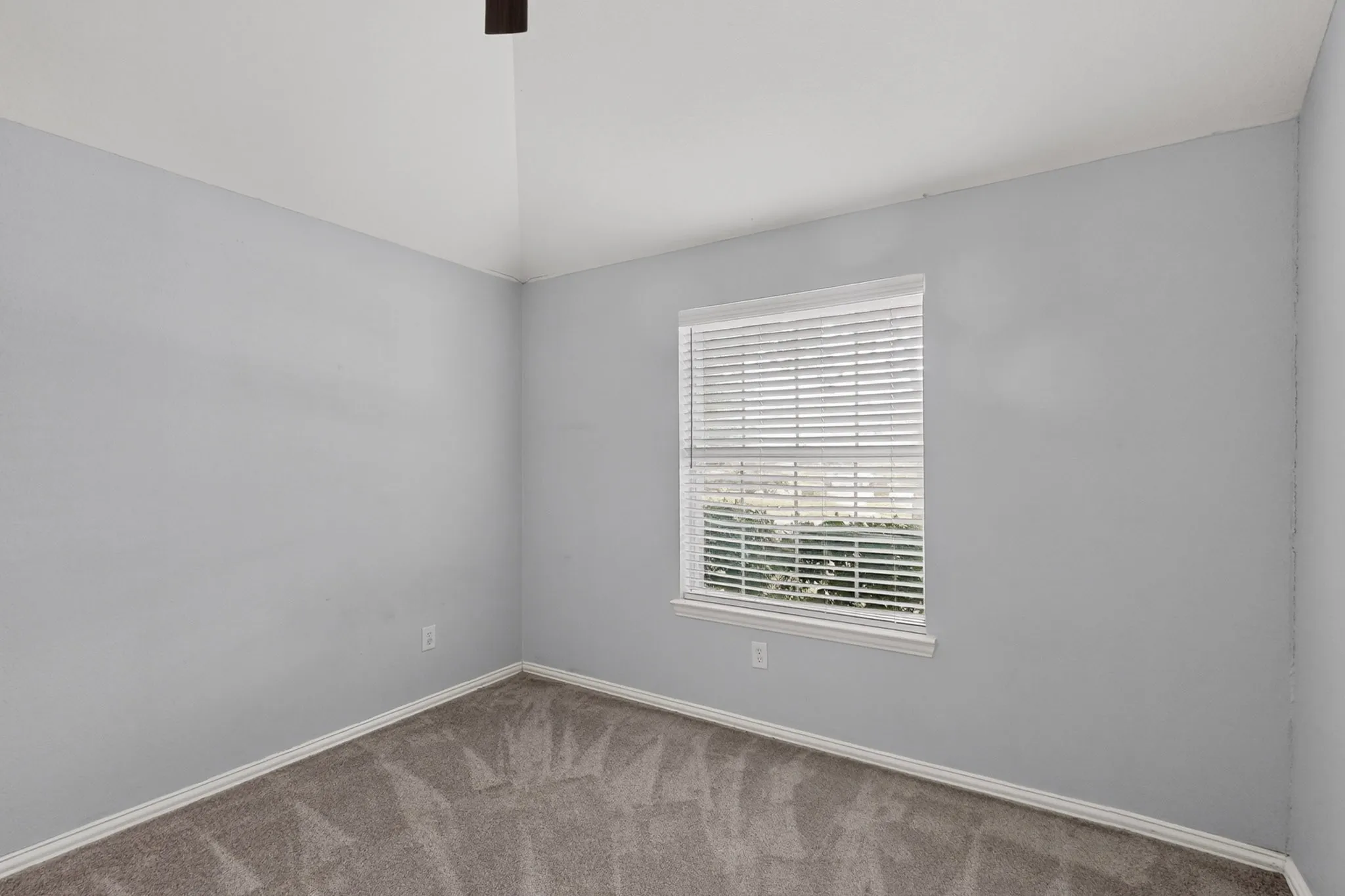 Vaulted ceiling with a flush-mount light fixture, a window with horizontal blinds, and neutral carpeting