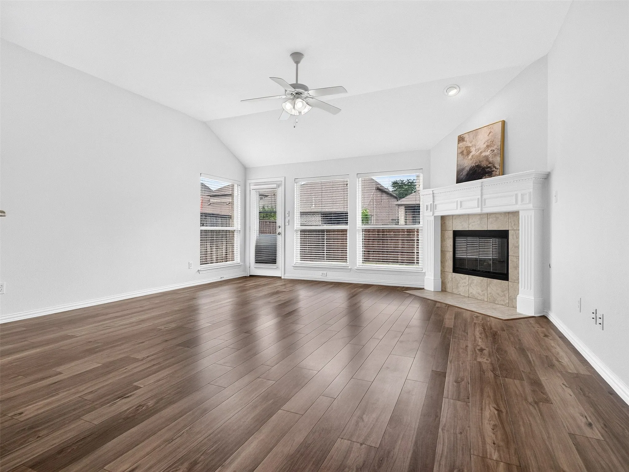 Vaulted ceiling, wood-finish flooring, corner fireplace with decorative mantel, ceiling fan, and multiple windows