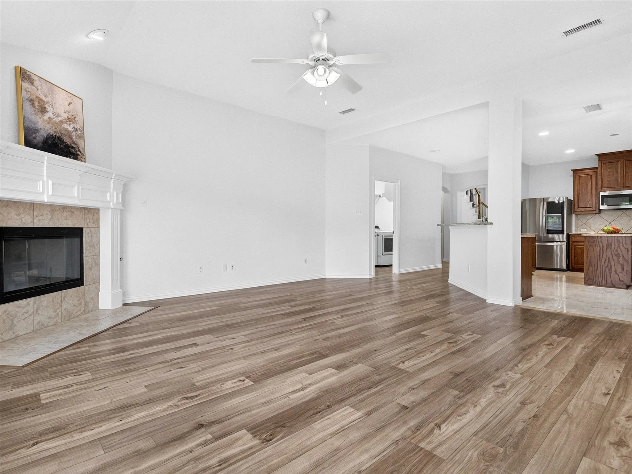 Spacious living area featuring wood-finish flooring, a fireplace with a stone surround, and an overhead ceiling fan