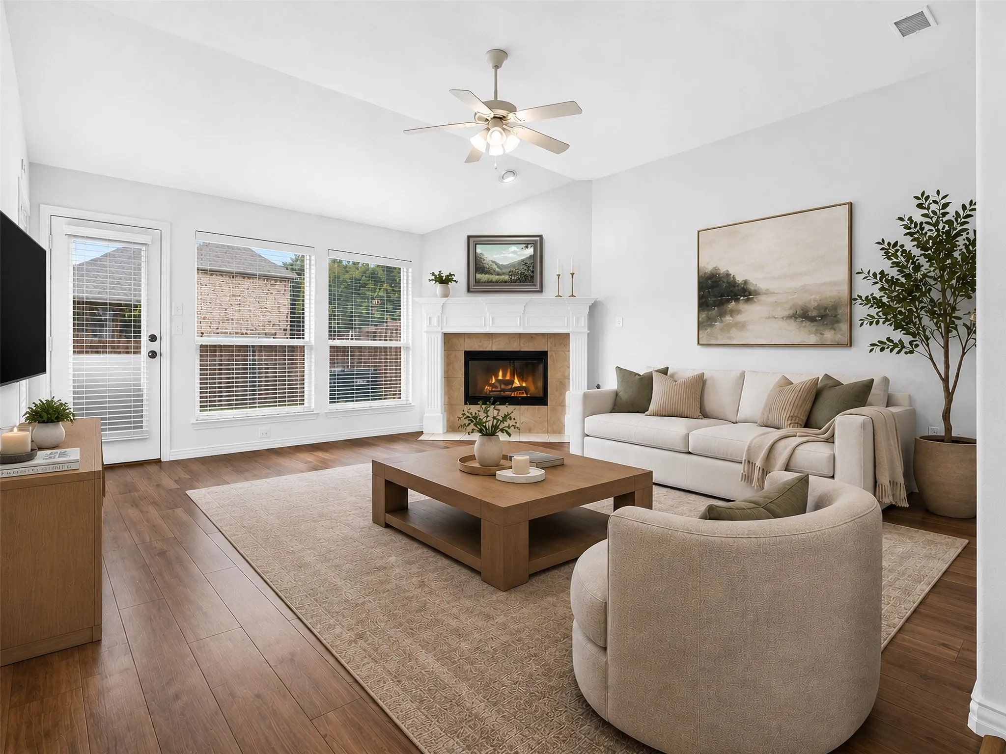 Vaulted ceiling with a ceiling fan, fireplace with a tile surround and mantel, wood-finish flooring, and multiple windows