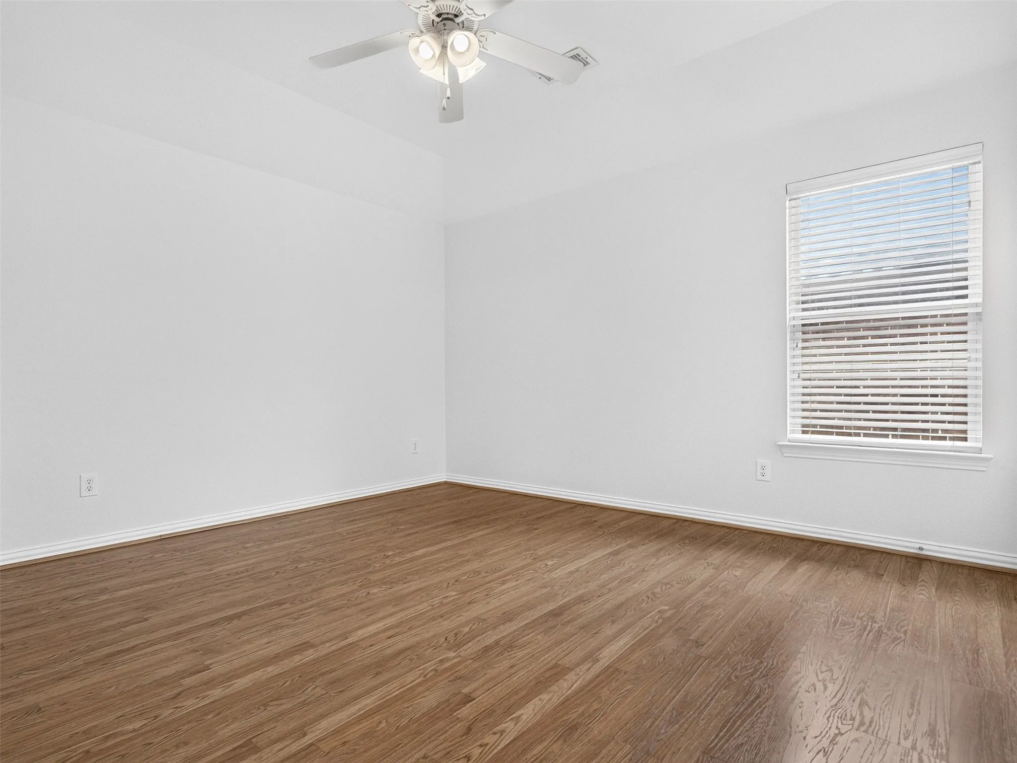 Vaulted ceiling, wood-finish flooring, white walls, single window with blinds, and a ceiling fan with integrated lighting