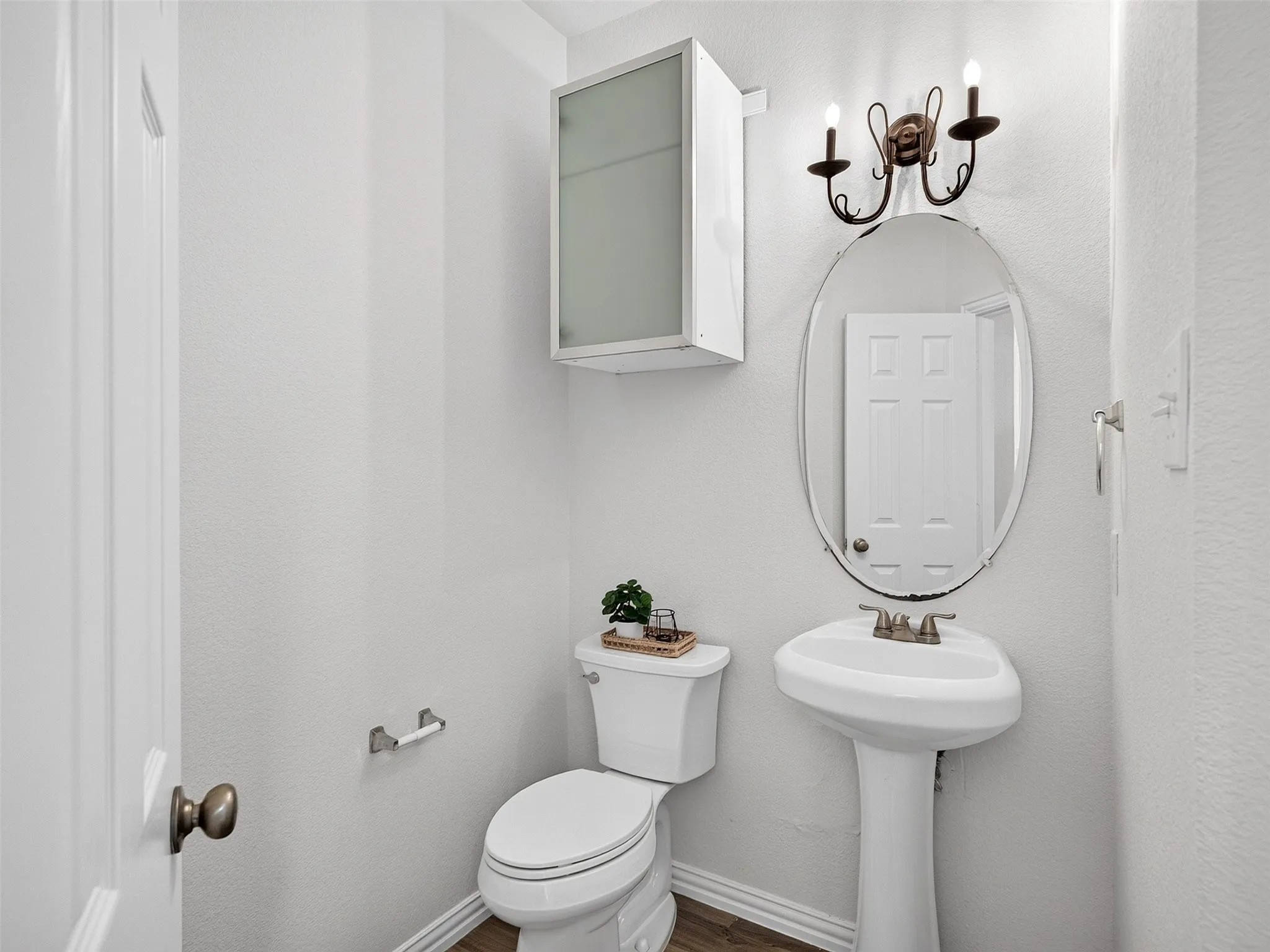 Pedestal sink with an oval mirror, wall-mounted light fixture, and wood-finish flooring