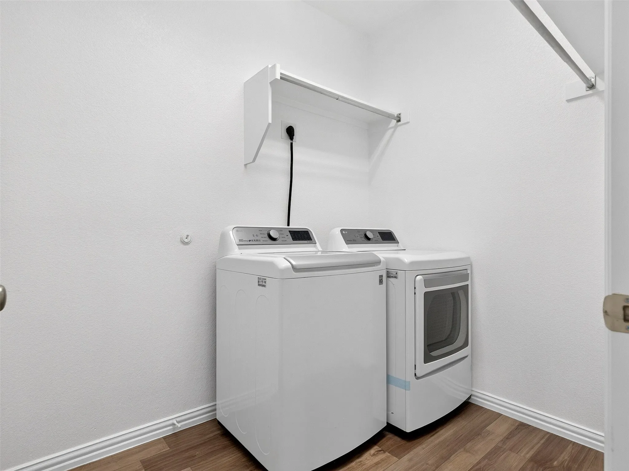 Dedicated laundry room featuring a top-load washer and front-load electric dryer with stacked configuration, wood-finish flooring, white painted walls, and a wall-mounted drying rack for air-drying delicate items