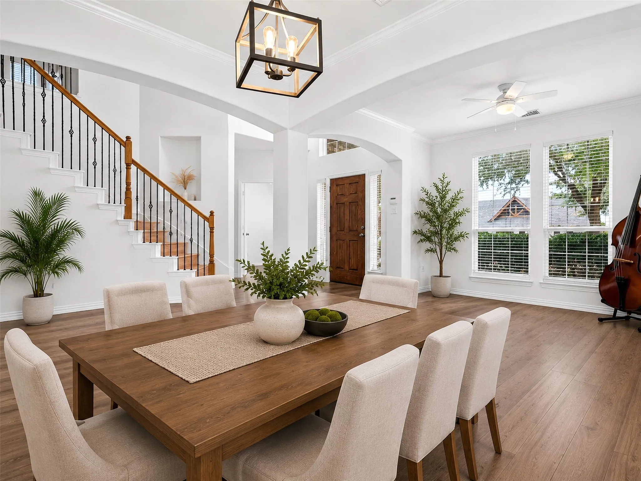 Wood-finish flooring throughout, prominent staircase with wood handrail and black iron balusters, white crown molding, recessed wall niche, and a dark wood paneled entry door