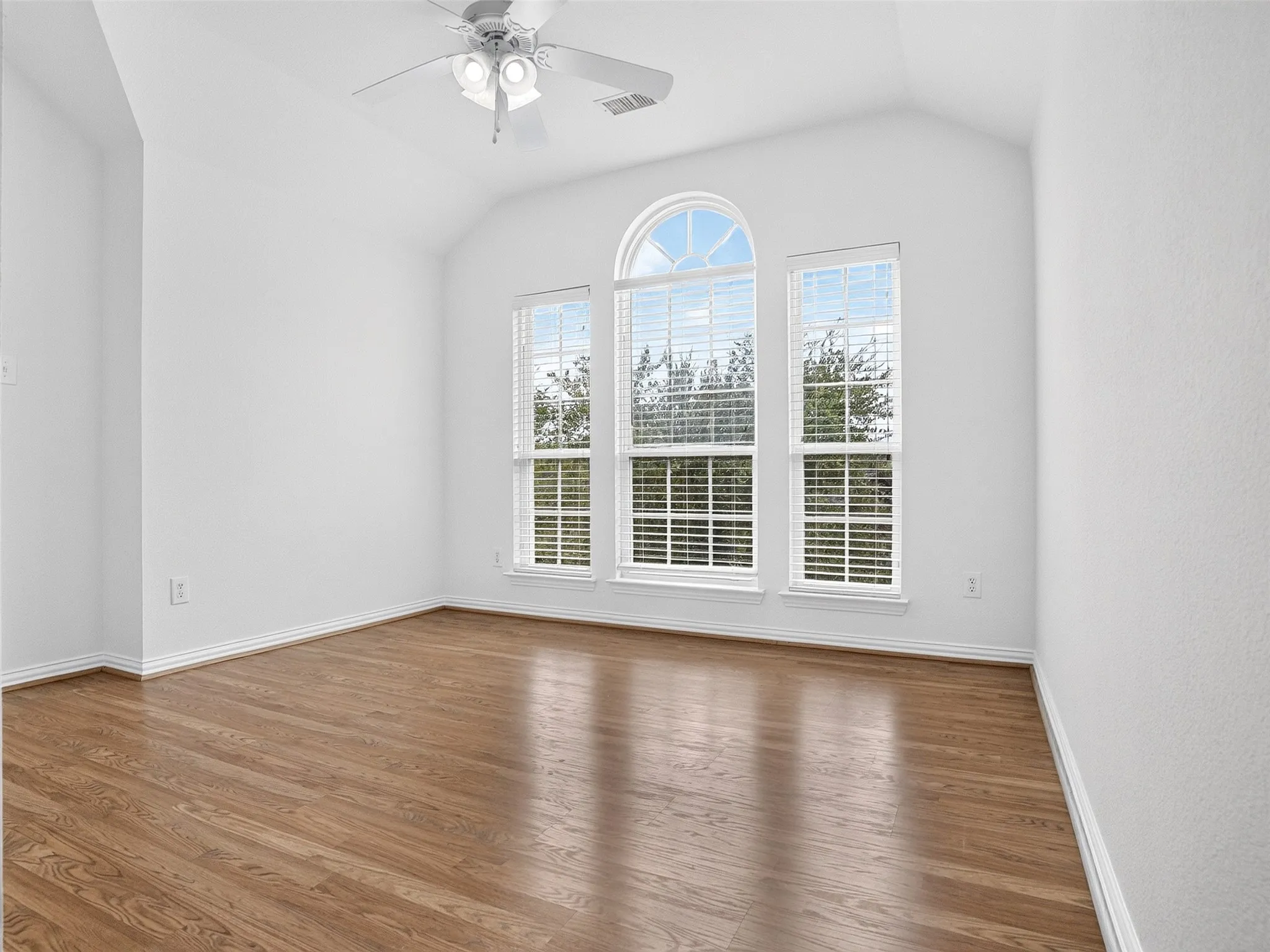 Vaulted ceilings, wood-finish flooring, a ceiling fan, and large arched windows with blinds