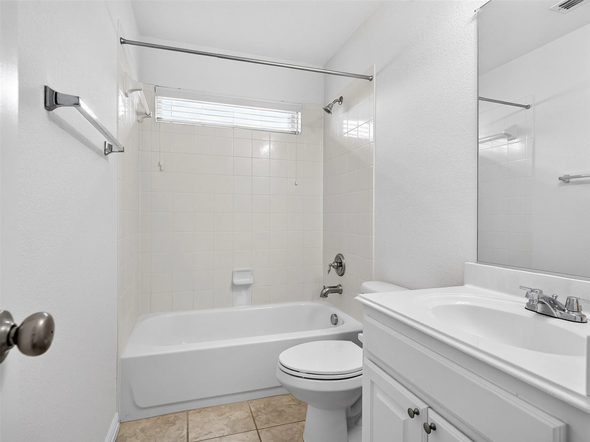 Bathroom featuring a white vanity with integrated sink, chrome faucet, white tile tub surround, and a horizontal privacy window