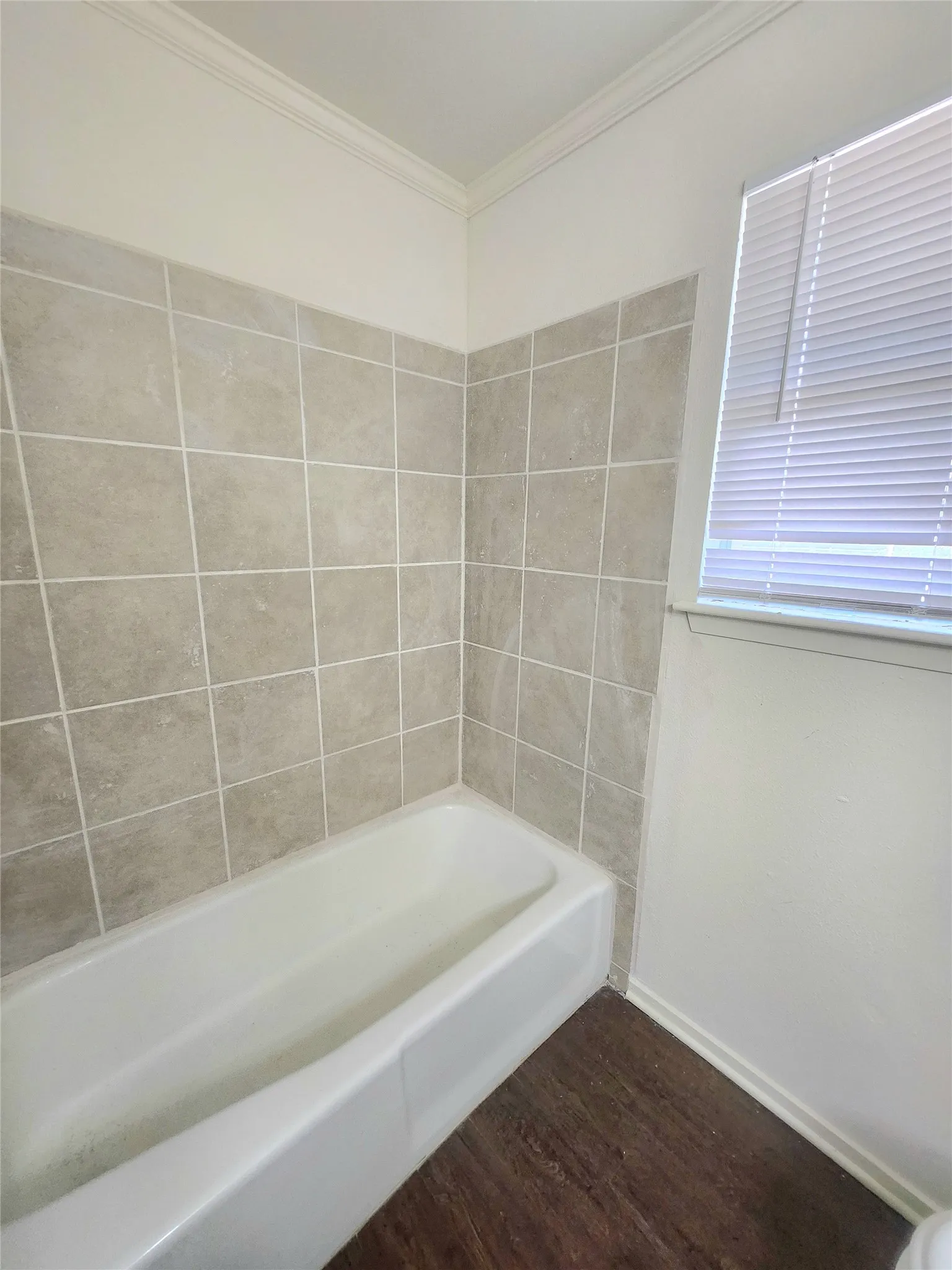 Bathtub with tile surround, wood-finish flooring, and crown molding