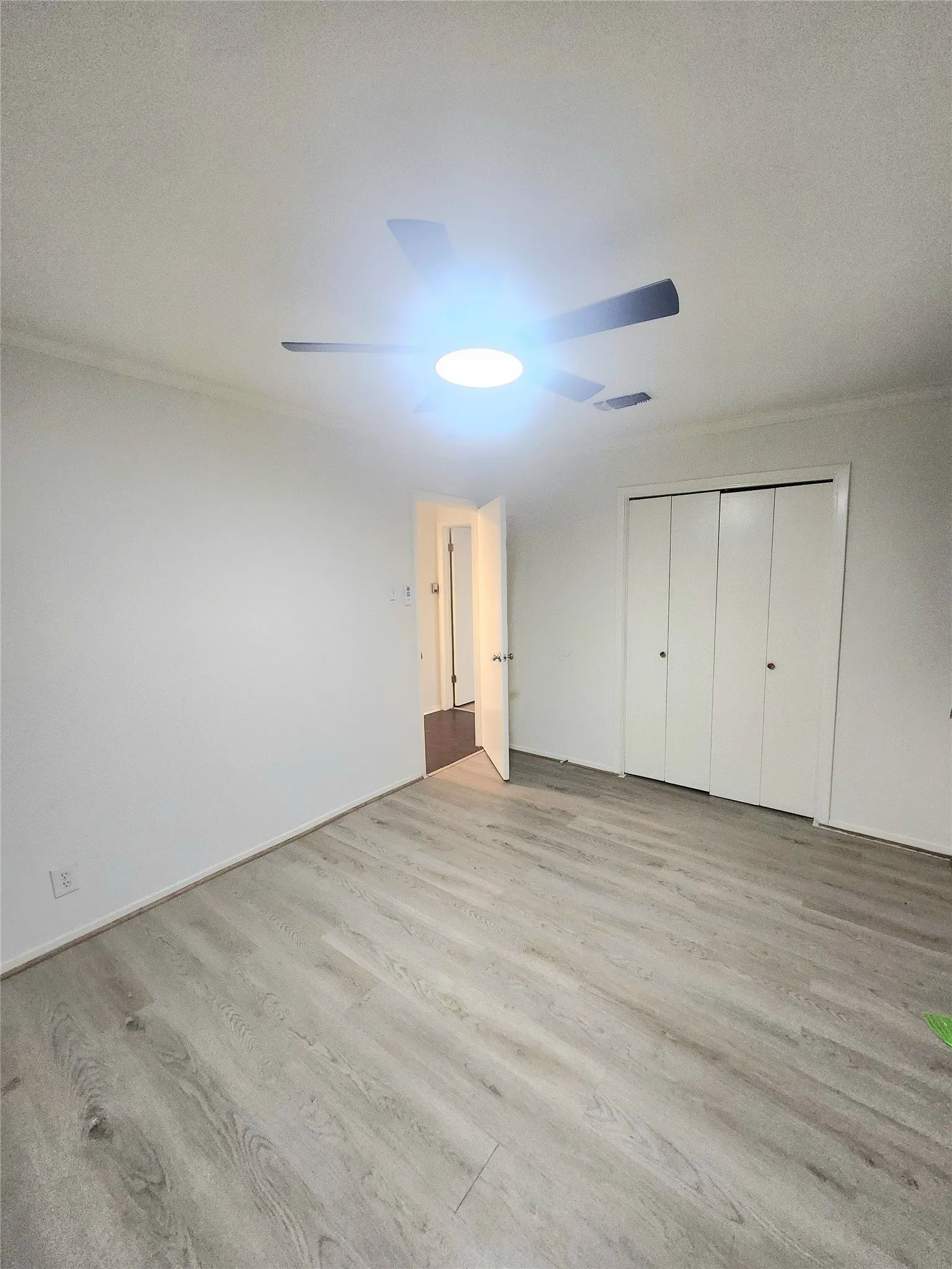 Wood-finish flooring with white walls, ceiling-mounted light fixture, and bifold closet doors
