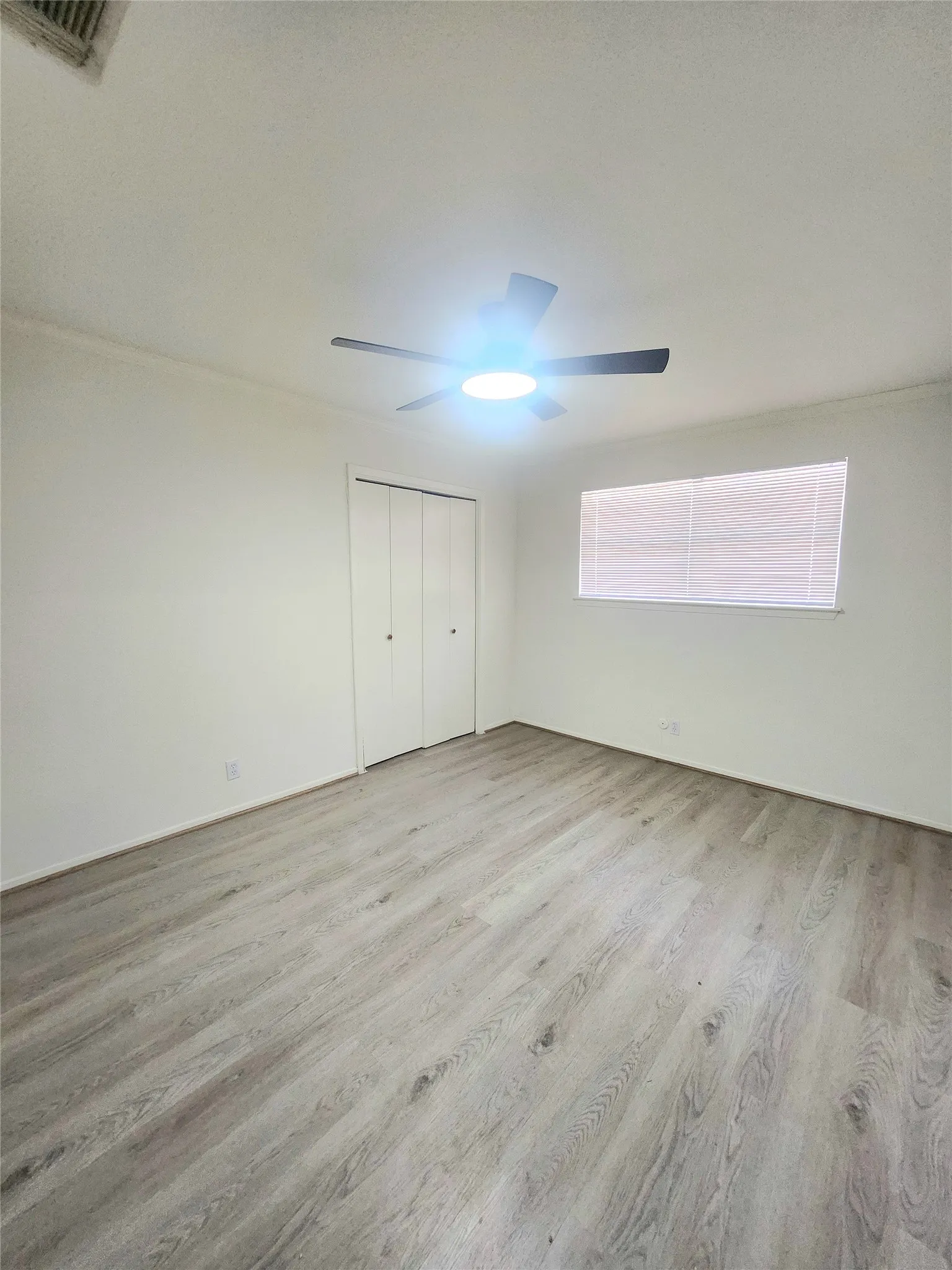 Wood-finish flooring, ceiling fan with integrated lighting, window with blinds, and bi-fold closet doors