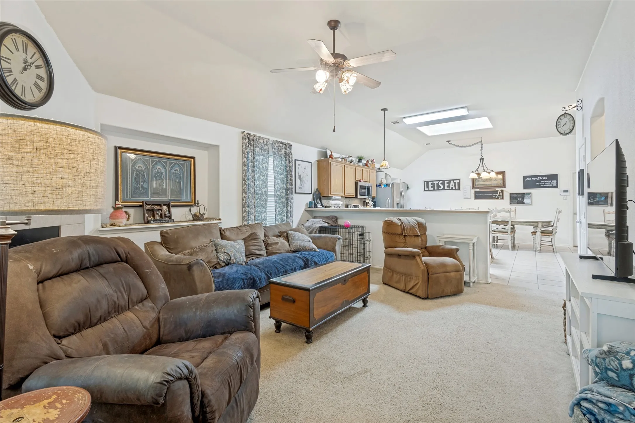 Vaulted ceiling with a ceiling fan, recessed fireplace, built-in shelving, kitchen with wood cabinetry, and a skylight