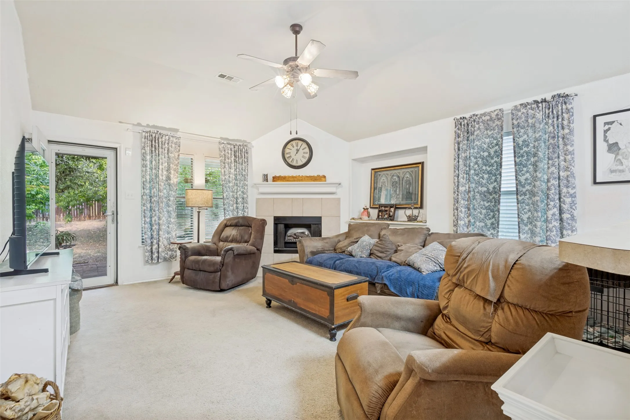 Vaulted ceiling living area featuring a wood buring fireplace with a mantel, ceiling fan, and carpeted flooring